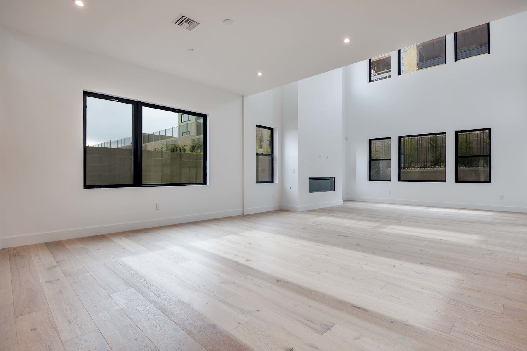 A spacious, minimalist room with large windows, hardwood floors, and framed artwork on the walls.