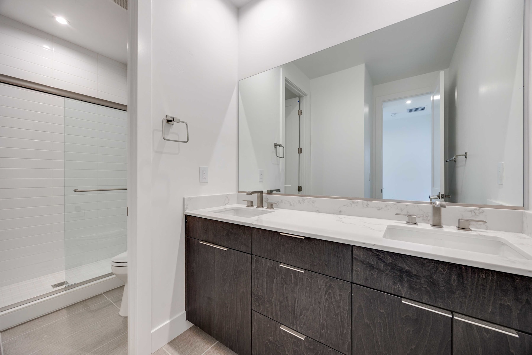 A modern bathroom with a dark wood vanity, white countertop, and a large mirror on the wall.