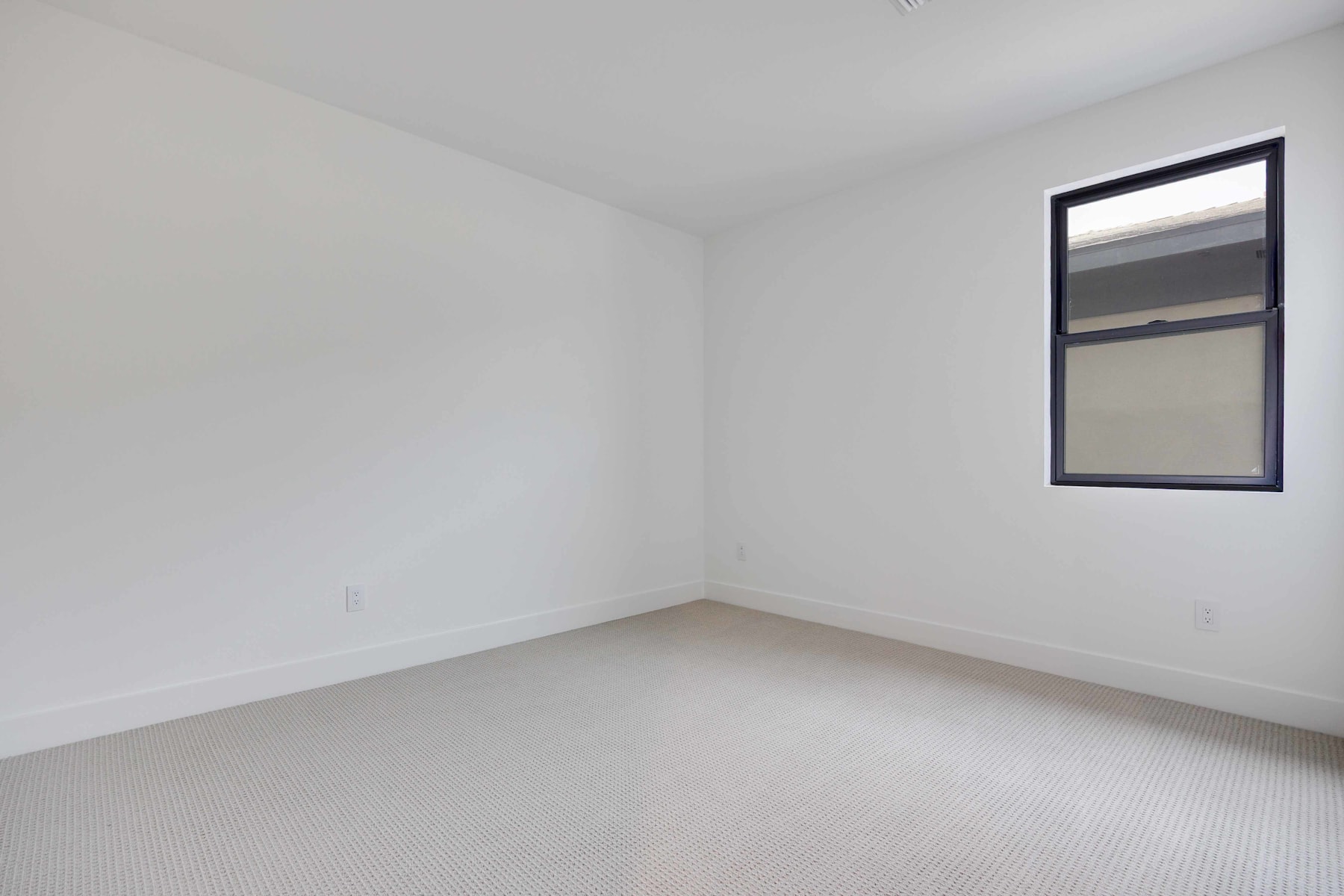 A simple, minimalist room with white walls, a small window, and a carpeted floor.