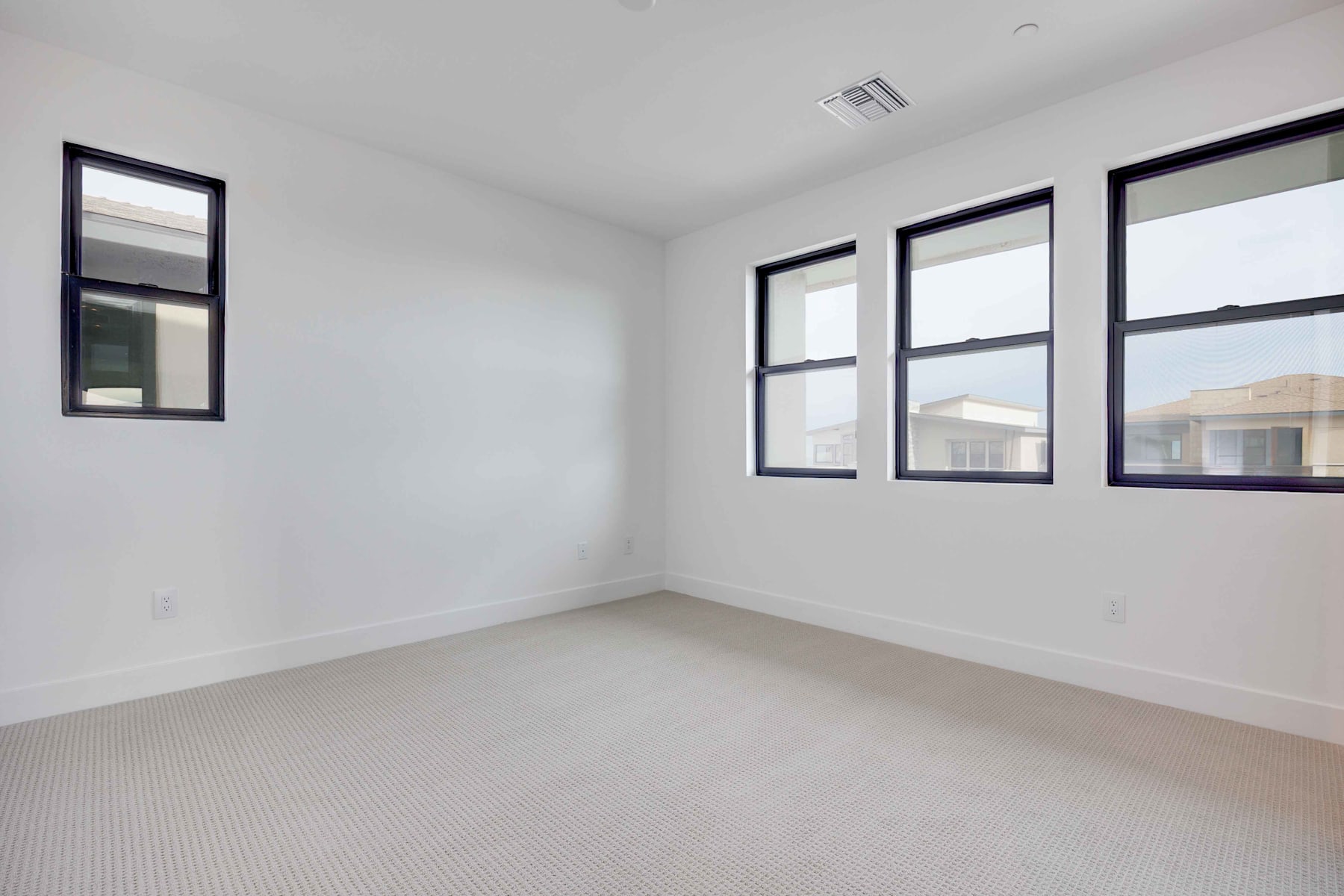 A spacious, well-lit room with white walls, large windows, and a carpeted floor.