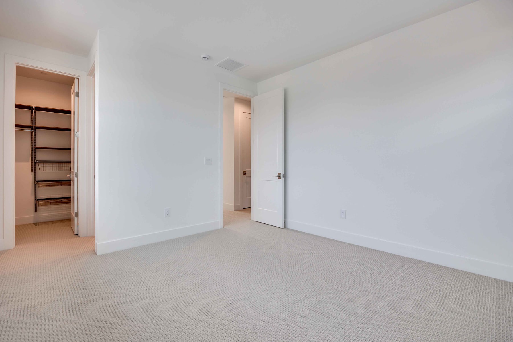 A spacious, minimalist bedroom with a built-in closet and a neutral-toned carpet covering the floor.