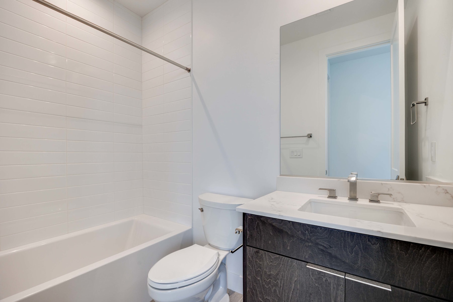 A modern bathroom with a white tiled wall, a dark vanity cabinet, and a mirror above the sink.