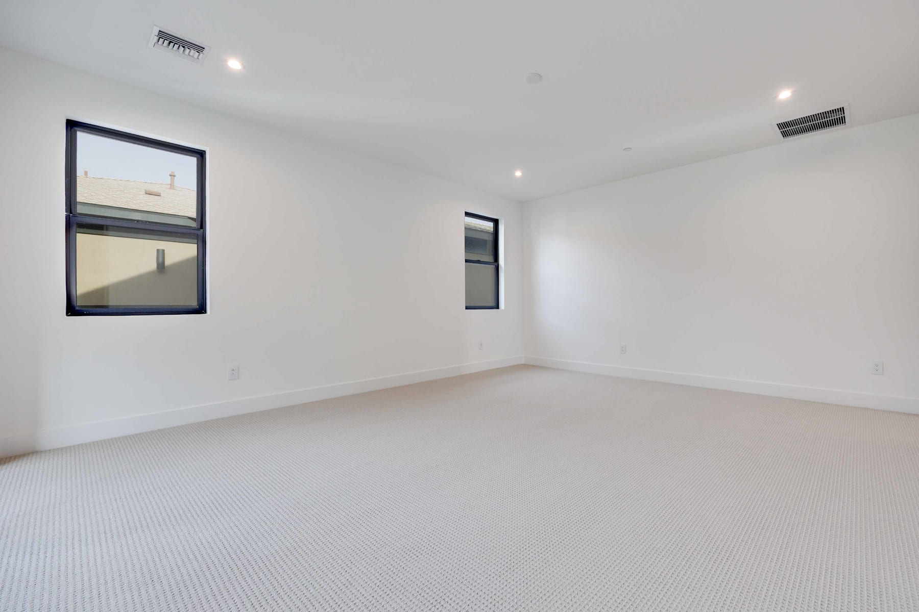 A spacious, minimalist room with white walls, a carpeted floor, and two framed artworks on the walls.