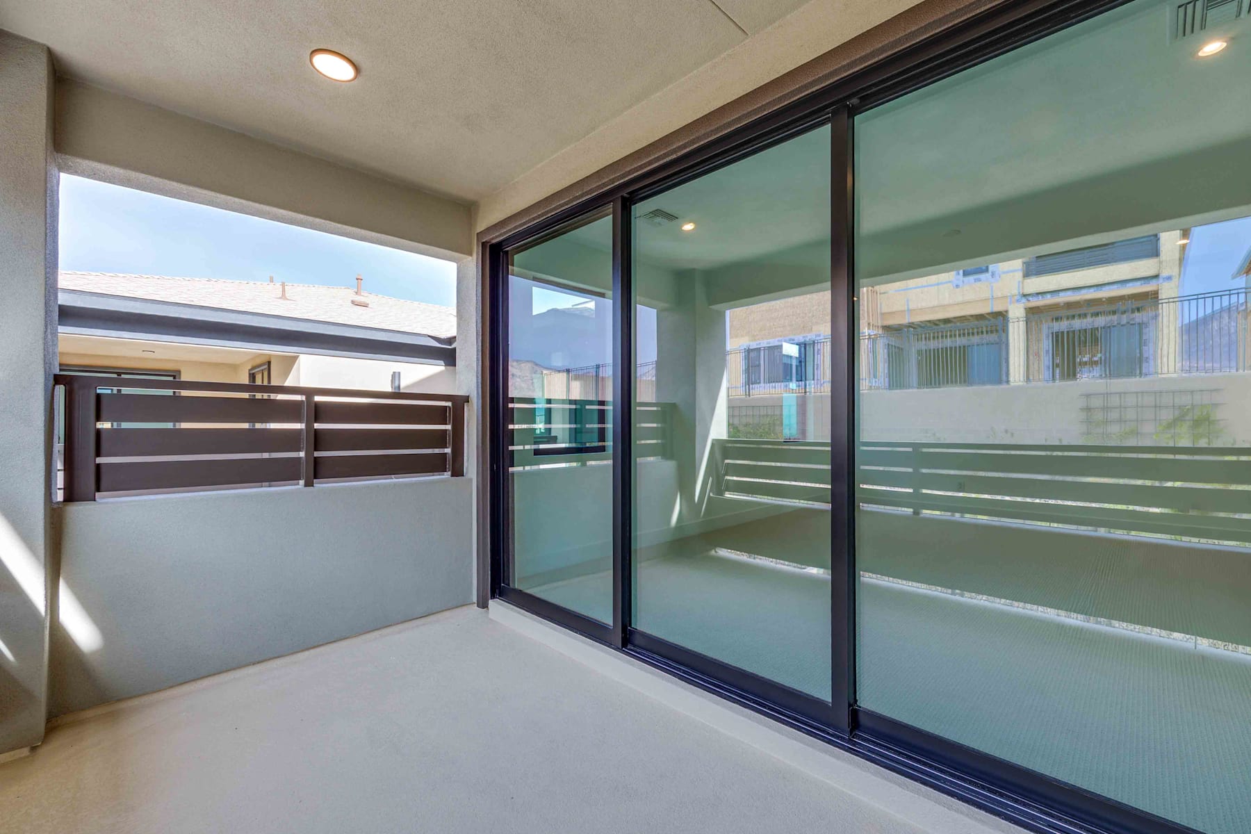 A modern, glass-enclosed balcony or patio with sliding doors and a metal railing, overlooking a residential or urban setting.