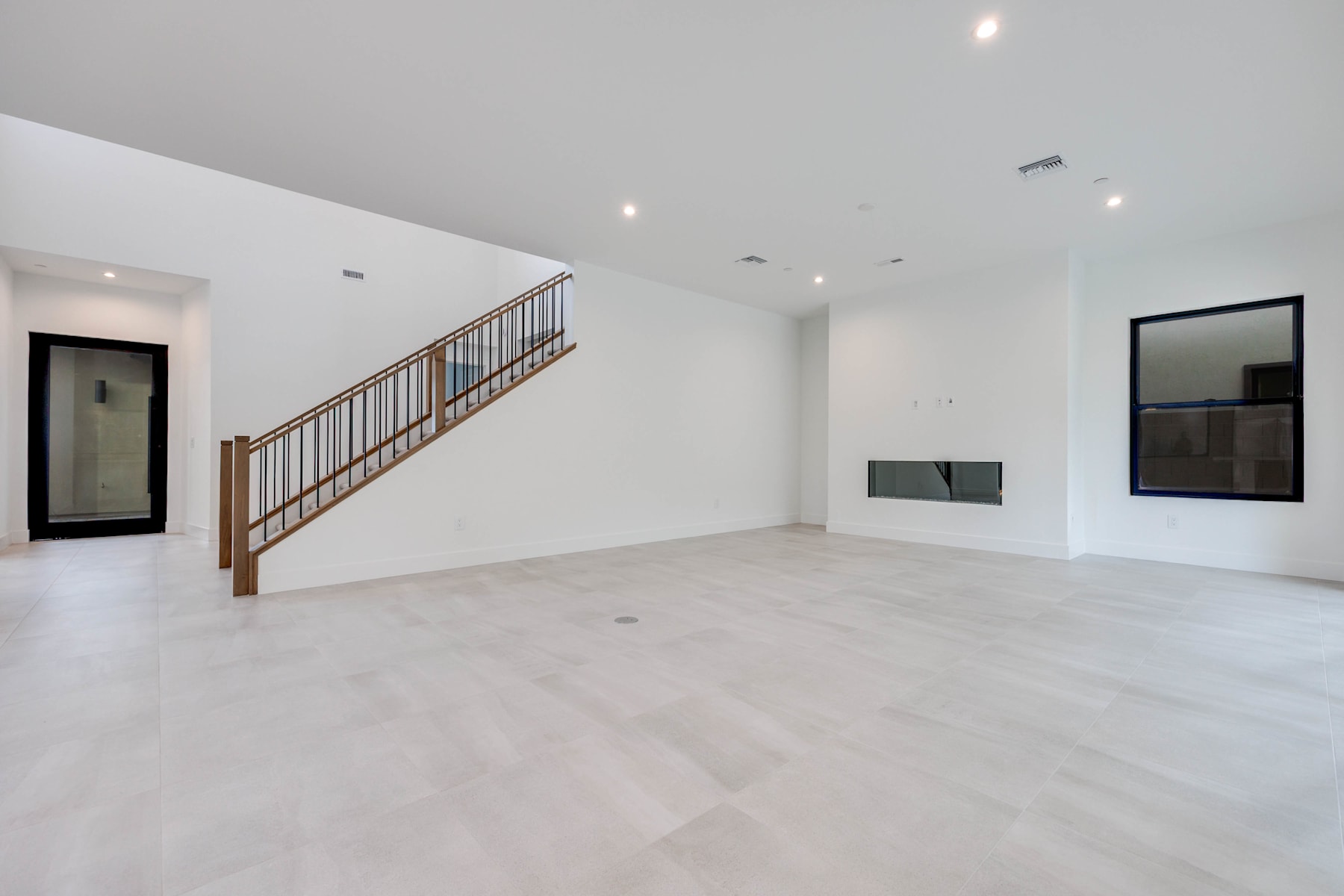 A spacious, minimalist interior with a wooden staircase, white walls, and a large open space.