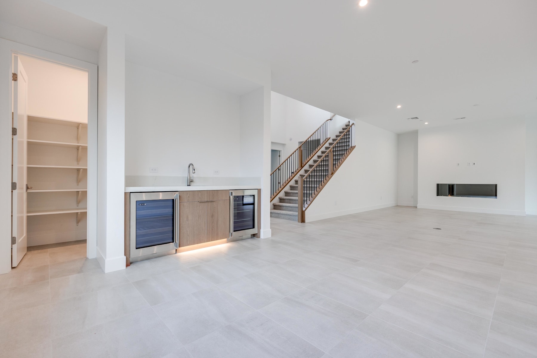 A spacious, open-concept living area with a kitchen, stairs, and a minimalist, modern design aesthetic.