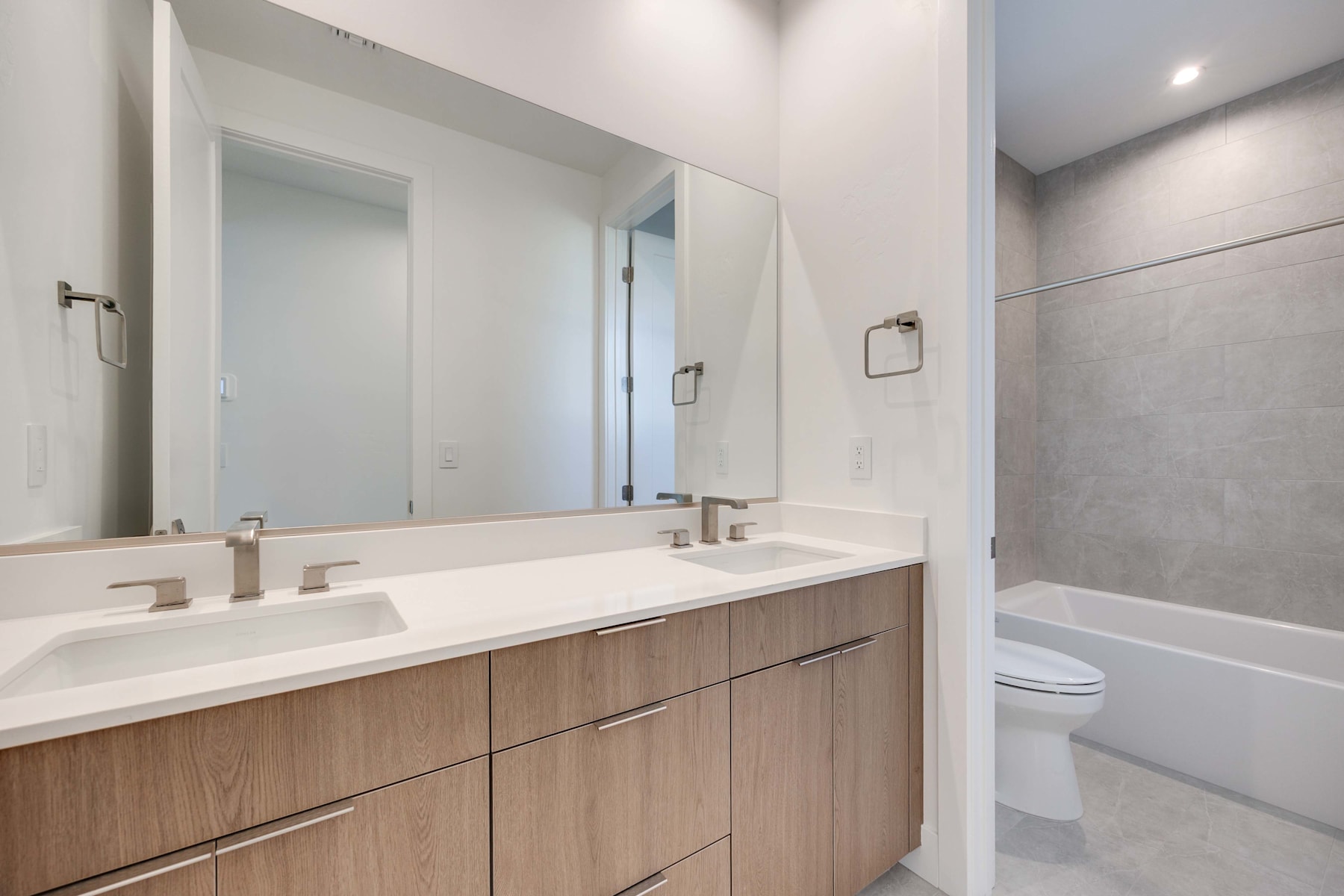 A modern bathroom with a double vanity, a large mirror, and a bathtub visible in the background.
