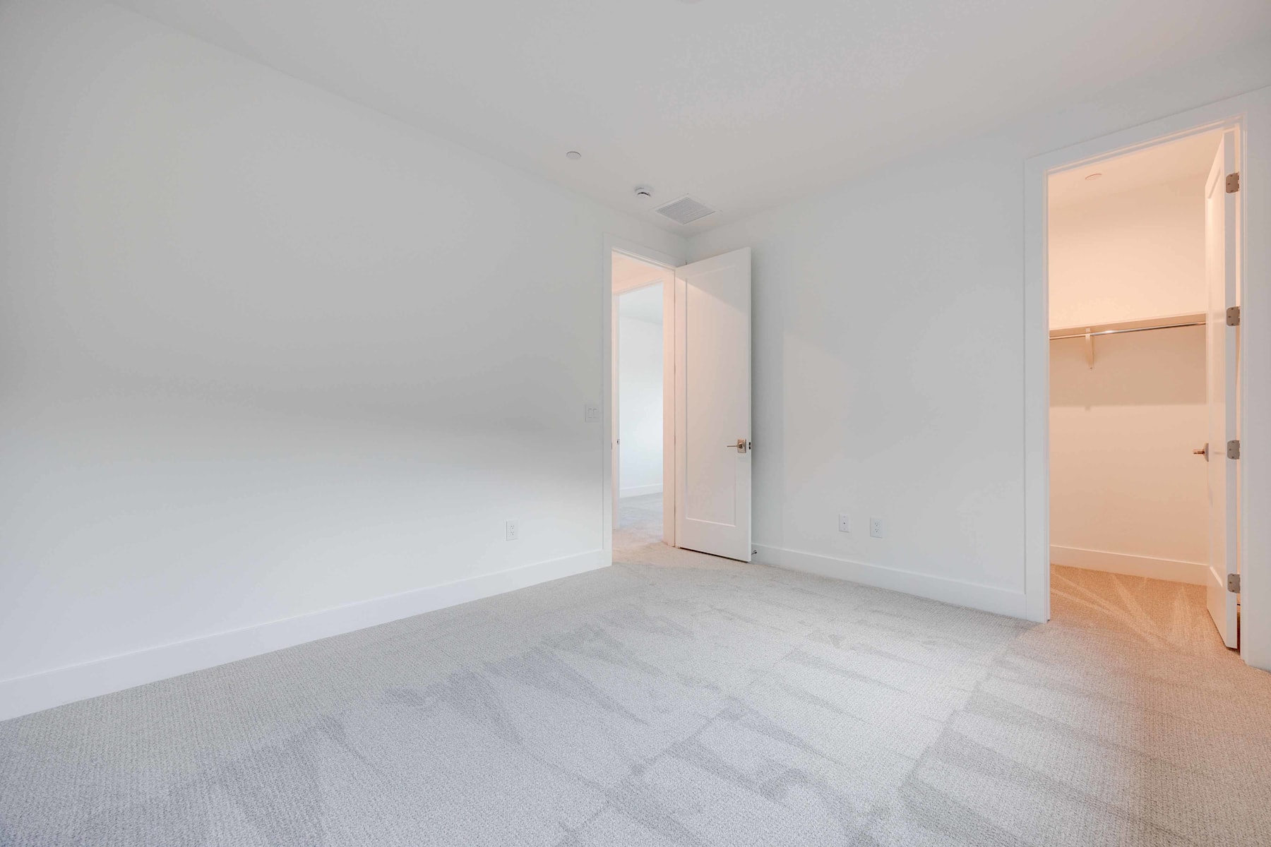 A bright, minimalist room with a white wall, wooden floor, and an open doorway leading to another room.