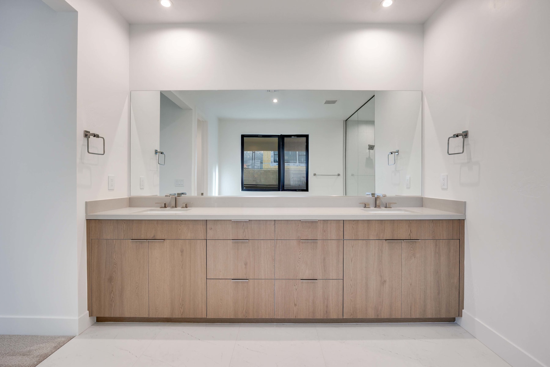 A modern and minimalist bathroom with a large vanity cabinet made of light-colored wood, a double sink, and a large mirror on the wall.