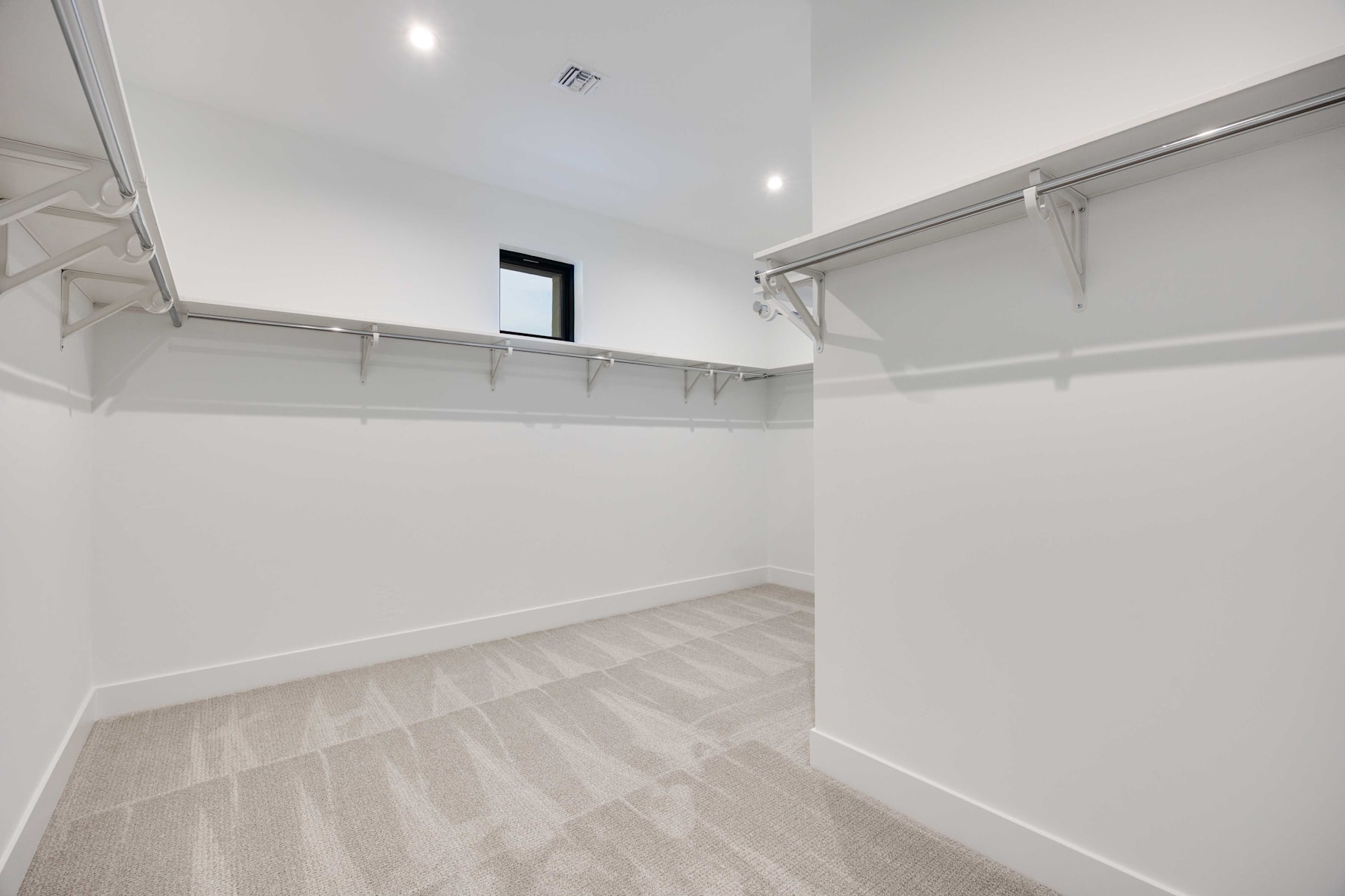 A bright, spacious walk-in closet with white walls, a high ceiling, and a wooden floor with a built-in shelving system along the walls.