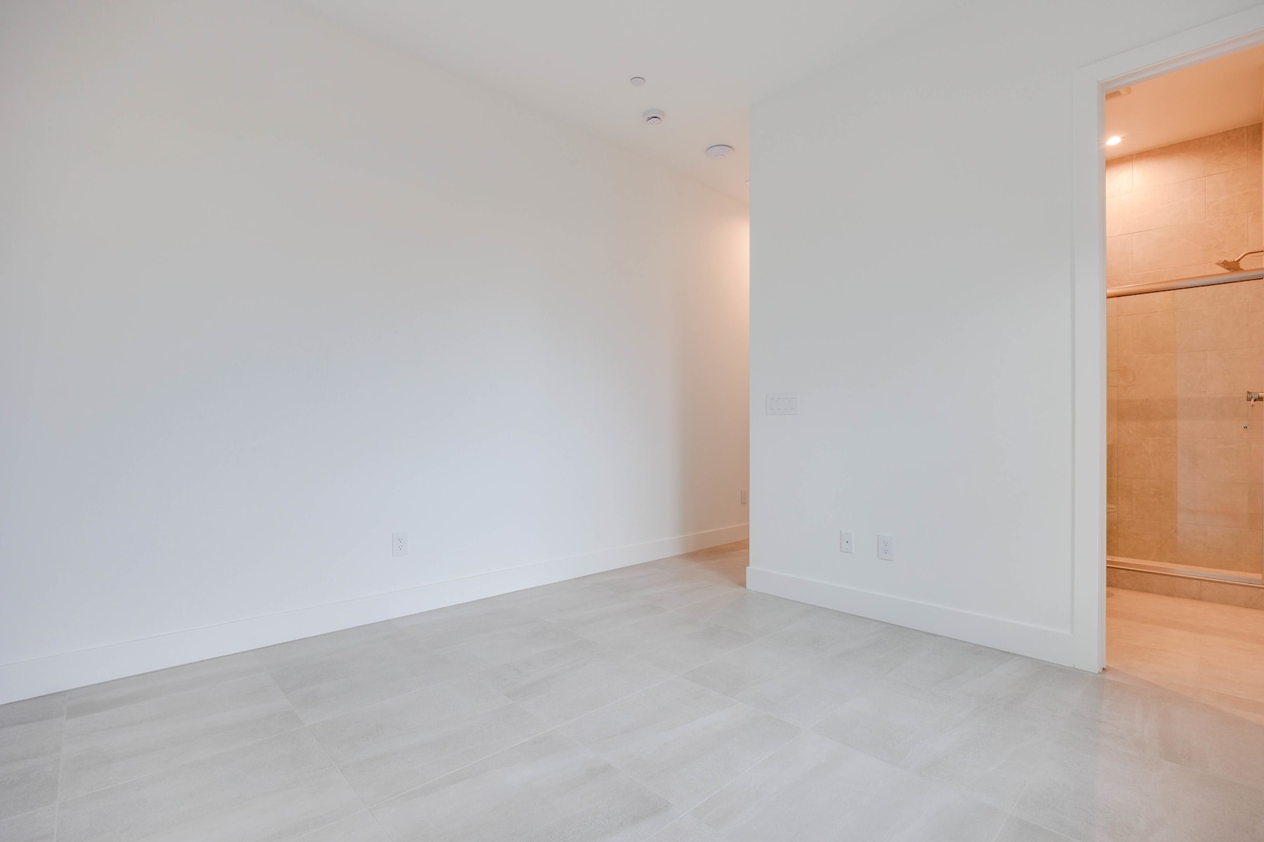 An empty, minimalist room with white walls and a gray concrete floor, featuring a doorway leading to another room.