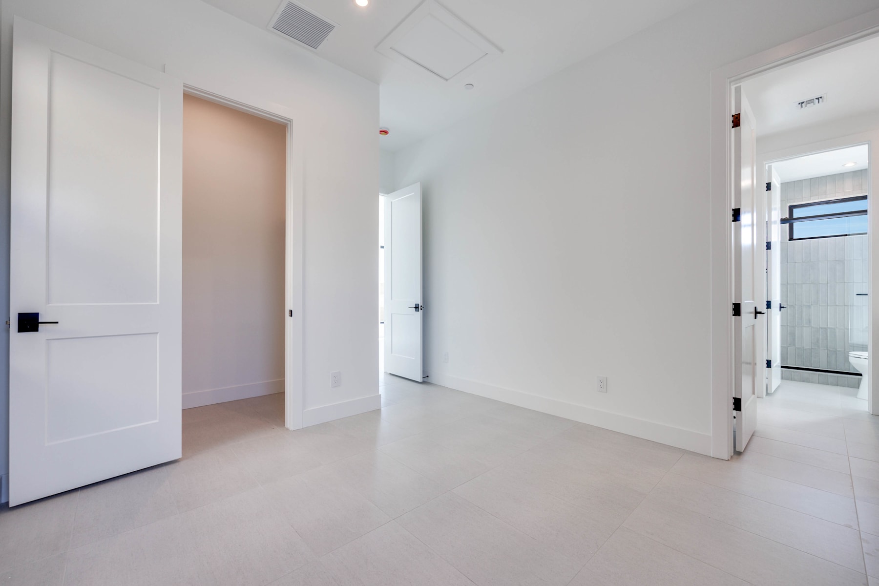 A spacious, minimalist room with white walls, a closed door, and an open doorway leading to another area.