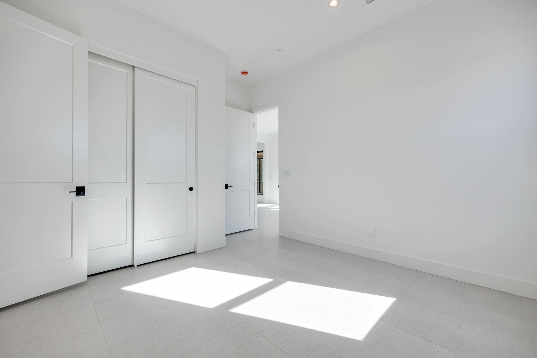 A bright, minimalist room with white walls, sliding doors, and natural light streaming in through the windows, creating a clean and airy atmosphere.