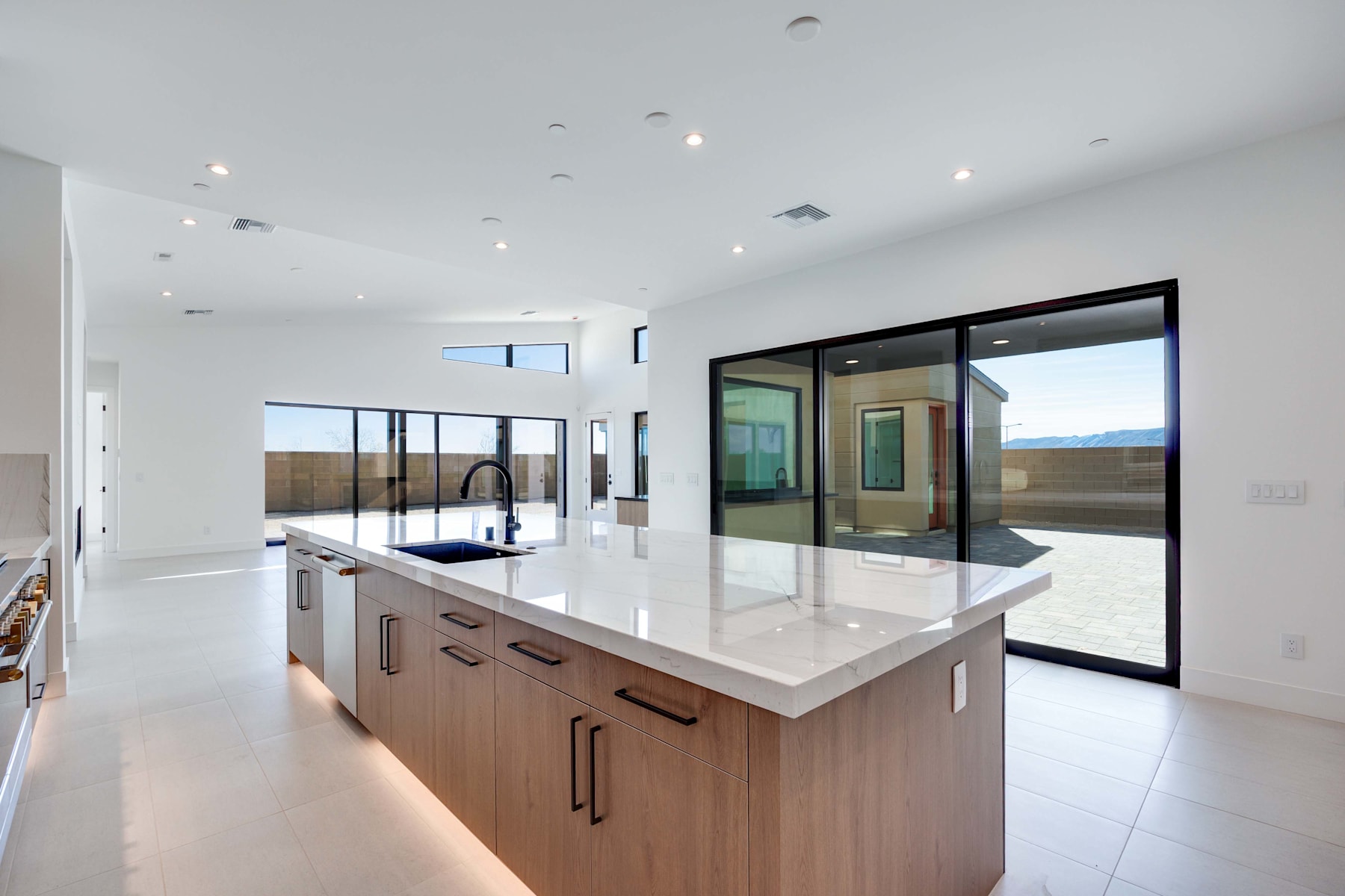 A modern, open-concept kitchen with a large island, wooden cabinets, and floor-to-ceiling windows providing a view of the outdoor landscape.