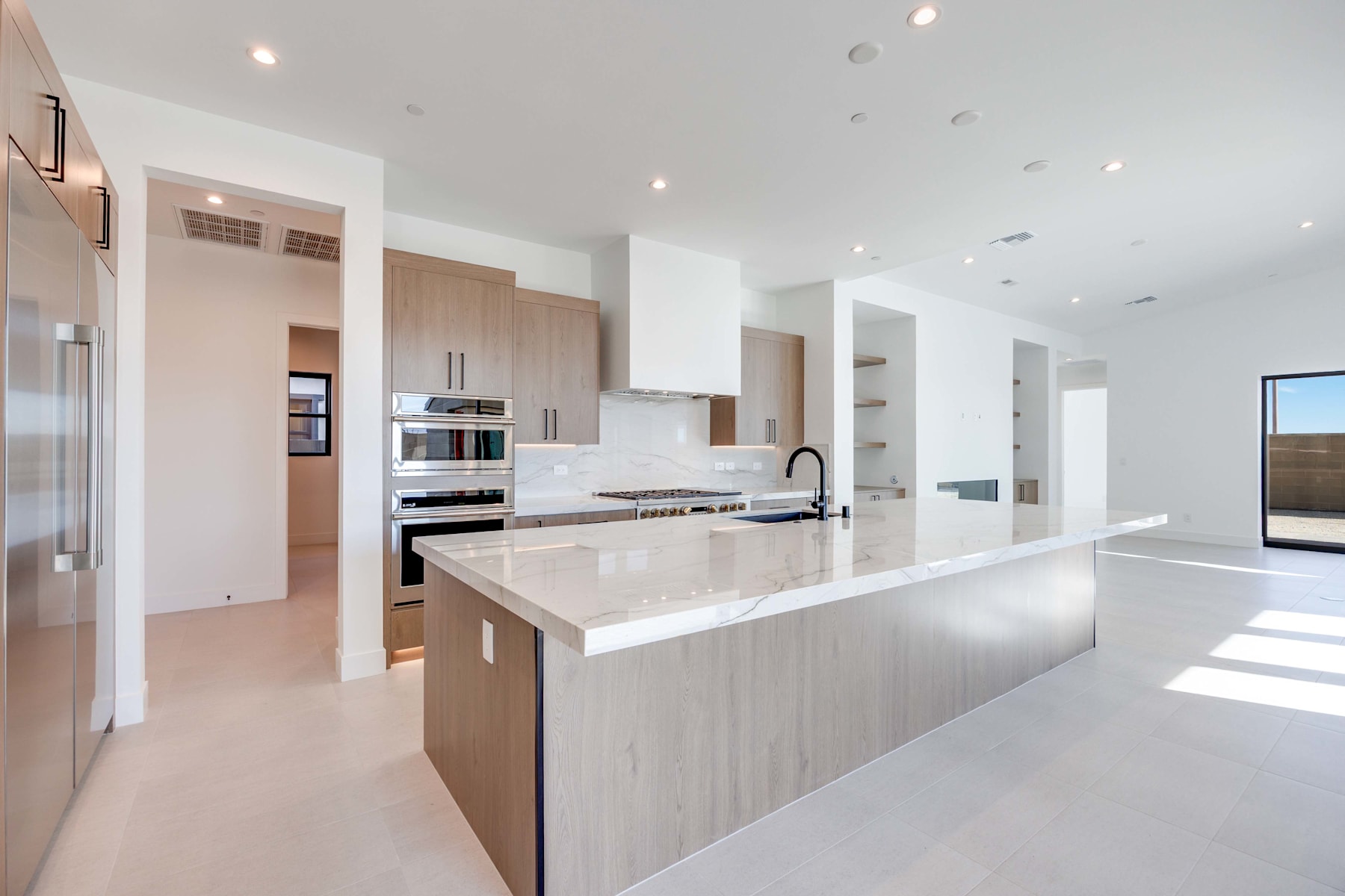 A modern, open-concept kitchen with white countertops, light-colored cabinets, and stainless steel appliances, set against a bright and airy background.