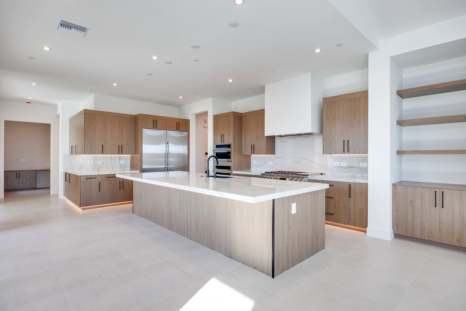 A modern, spacious kitchen with light-colored wood cabinets, a large central island, and a sleek, minimalist design.