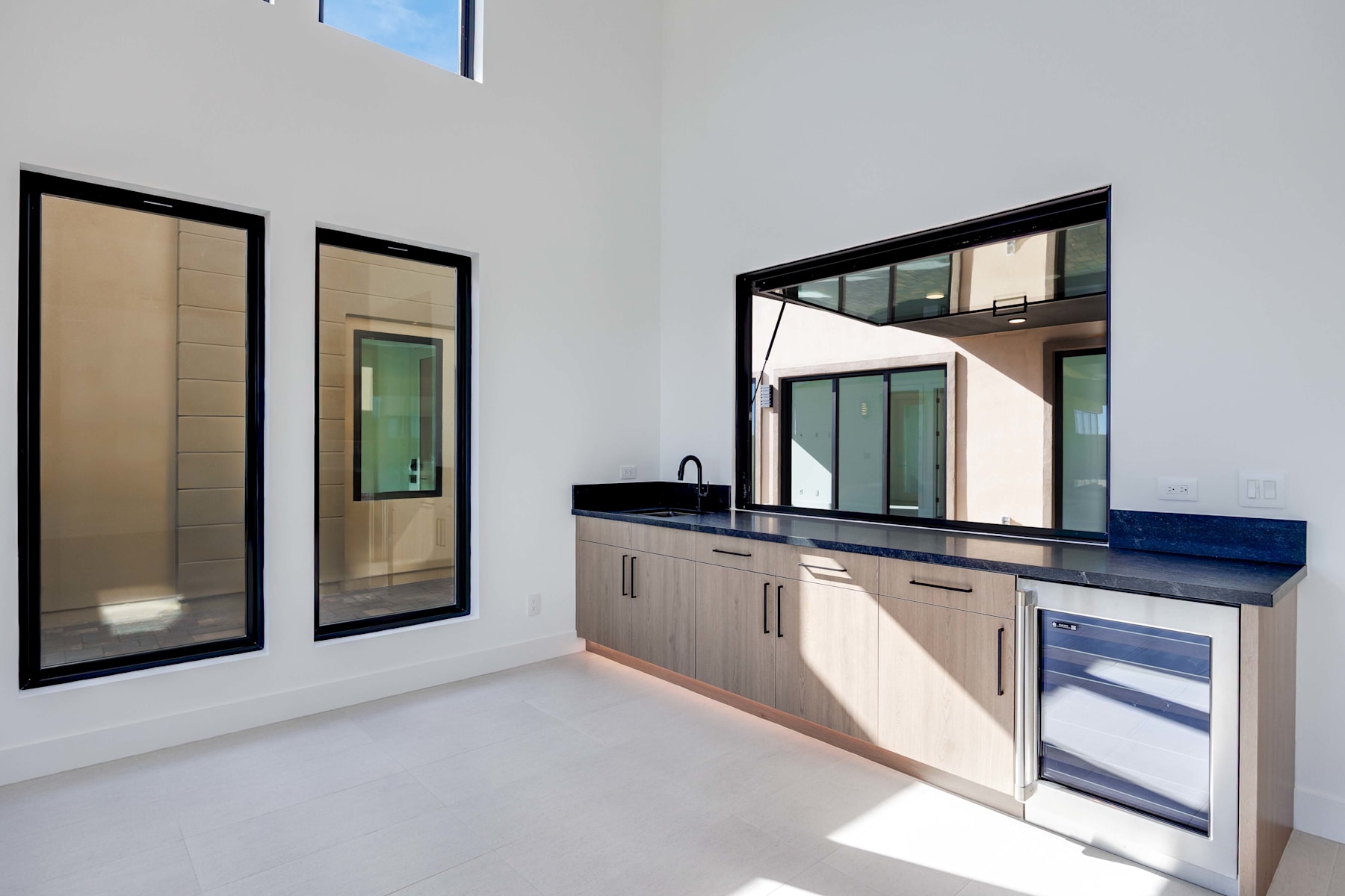 A modern, minimalist kitchen with sleek cabinets, a black countertop, and large windows providing ample natural light.
