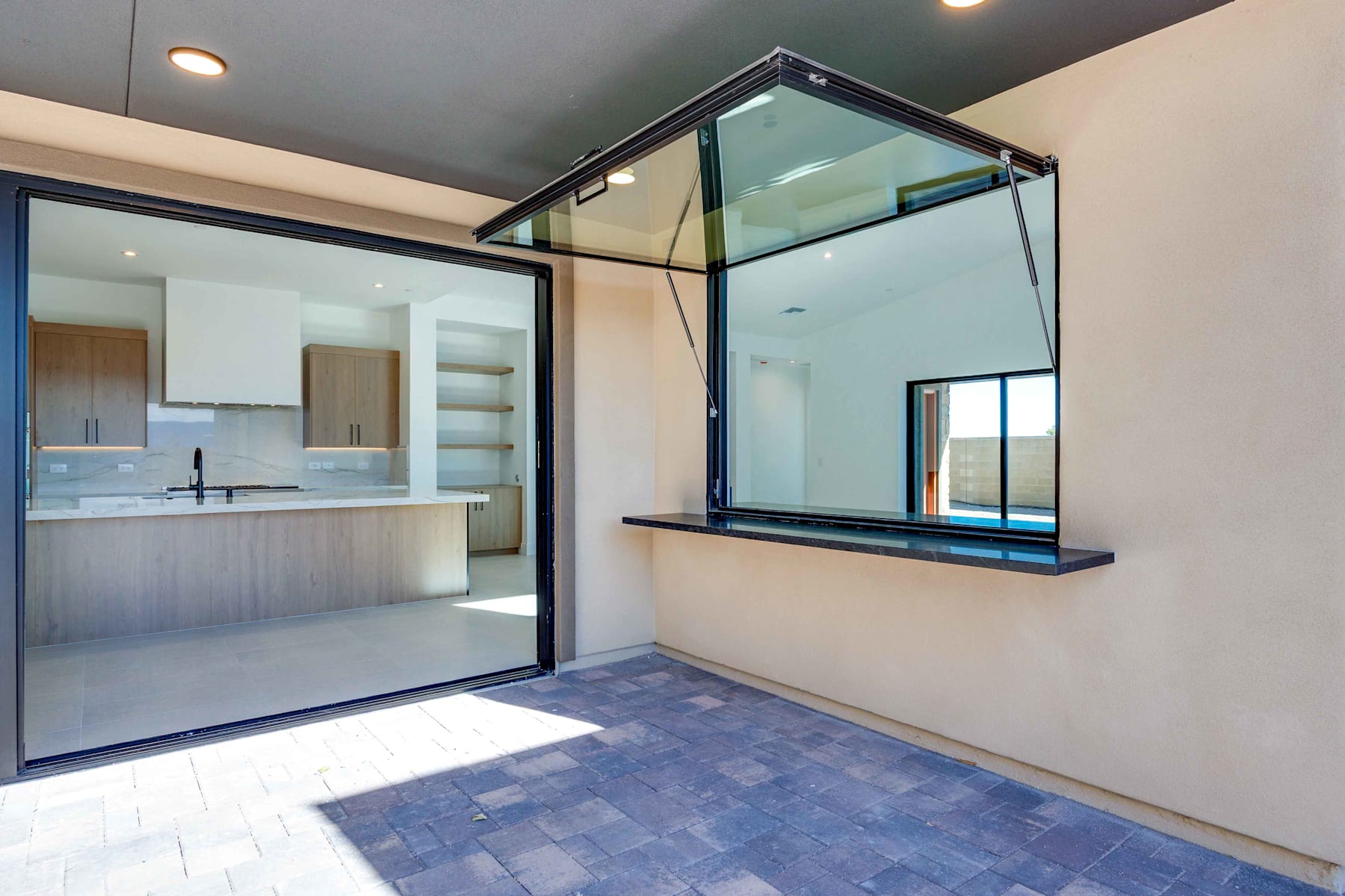 A modern, minimalist interior with a glass partition, a tiled floor, and a kitchen visible in the background.