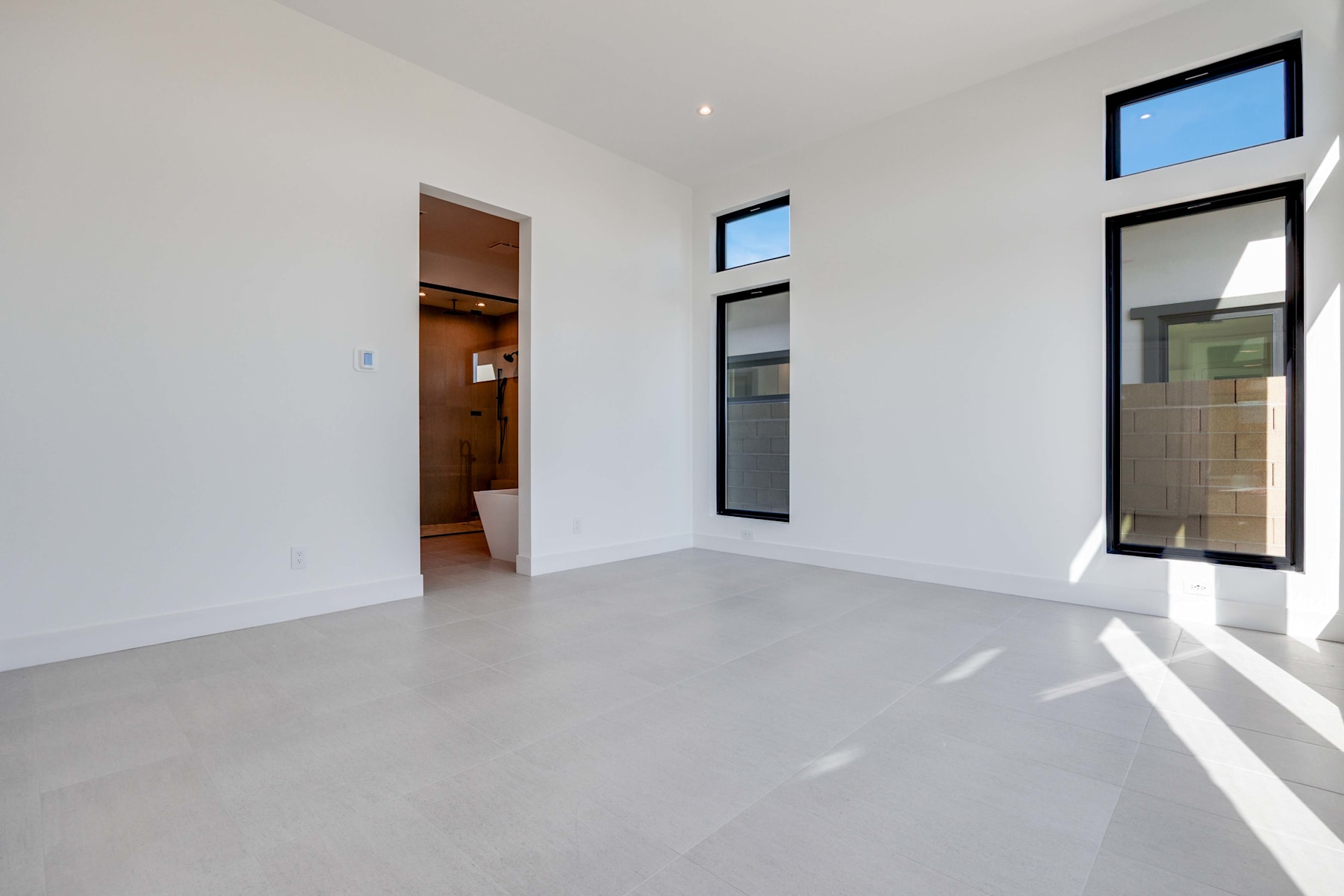 A spacious, minimalist room with white walls, large windows, and a concrete floor, creating a bright and airy atmosphere.