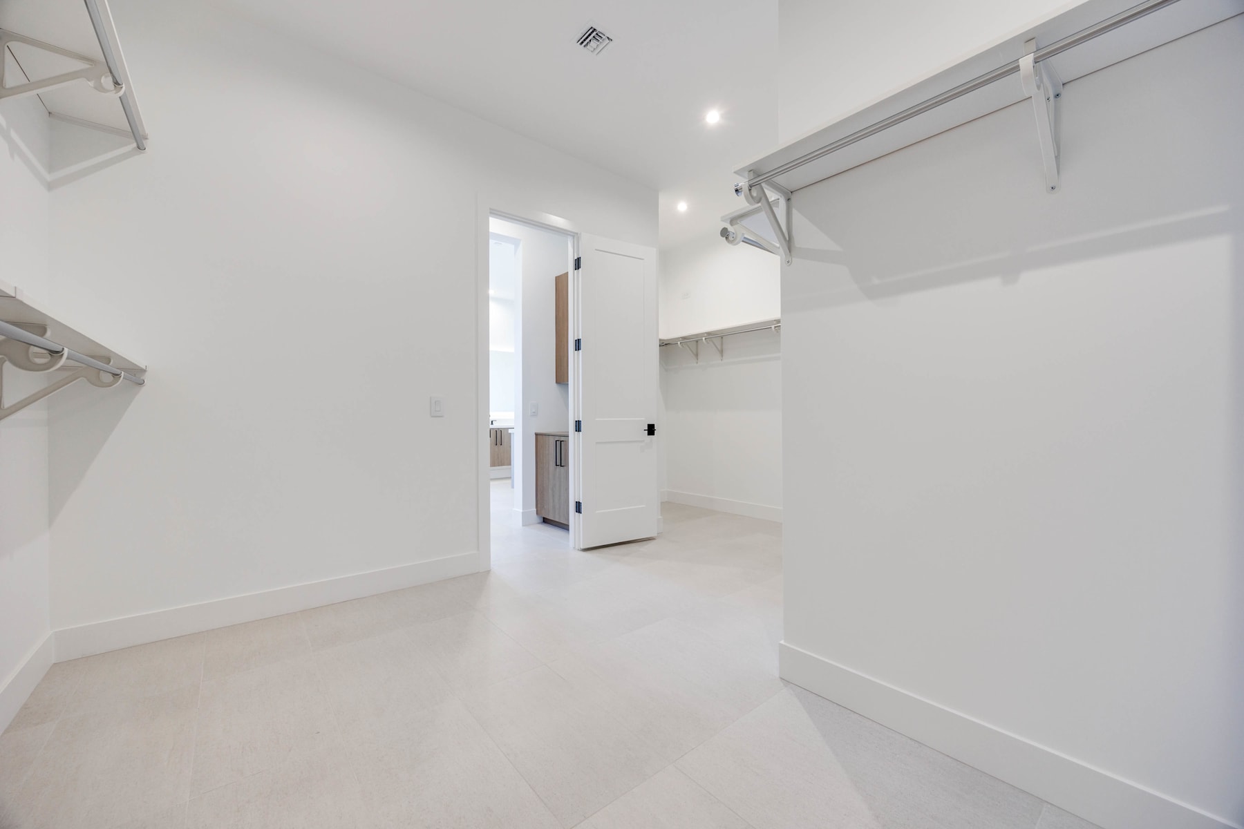 A bright, minimalist interior with a clean, white color scheme, featuring a hallway with built-in closets and a doorway leading to another room.