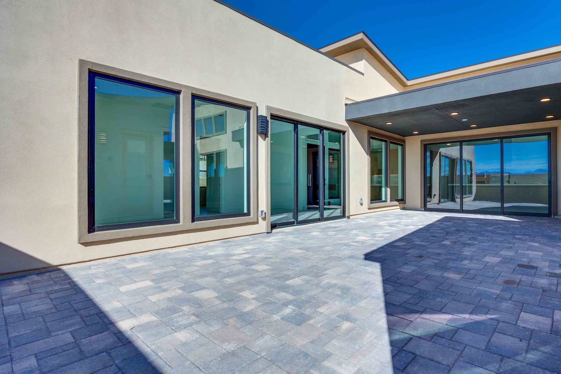 A modern, multi-story building with large glass windows and a paved outdoor area in the foreground, set against a clear blue sky.