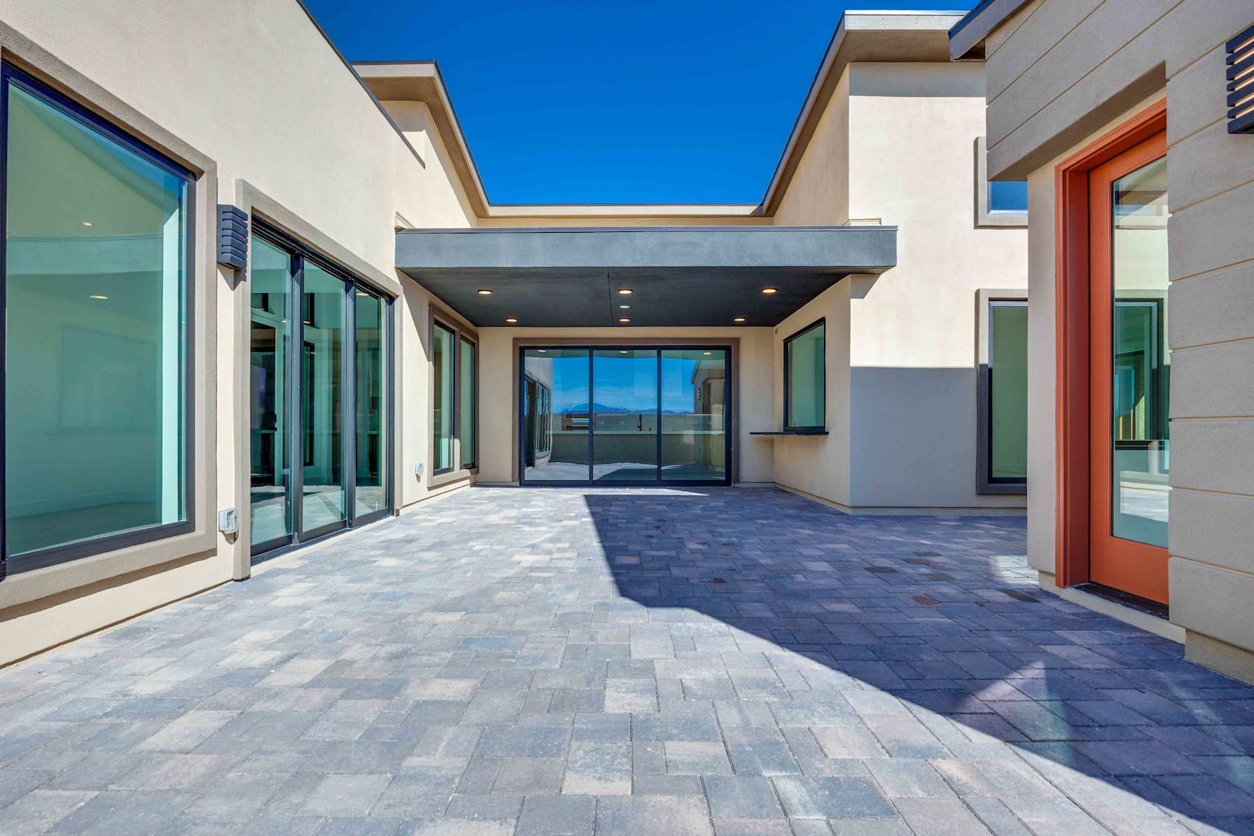 A modern, open-concept building with a paved walkway leading to a glass entryway, surrounded by a clear blue sky.