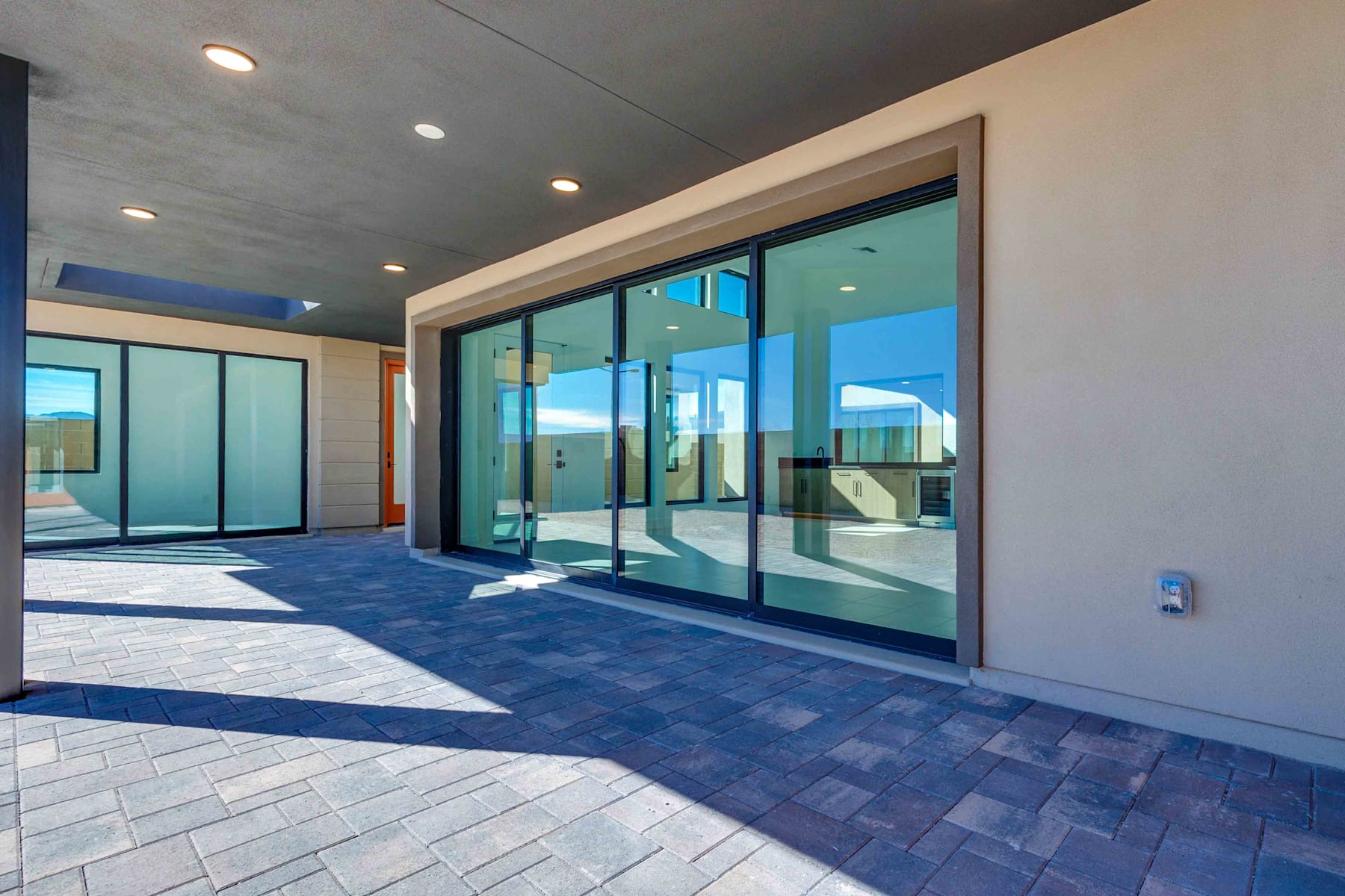 A modern, glass-enclosed entryway with a tiled floor and recessed lighting, leading to an open space beyond.