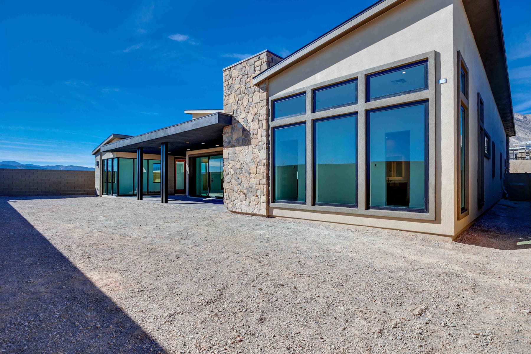 A modern, stone-clad building with large windows and a paved outdoor area, set against a clear blue sky.
