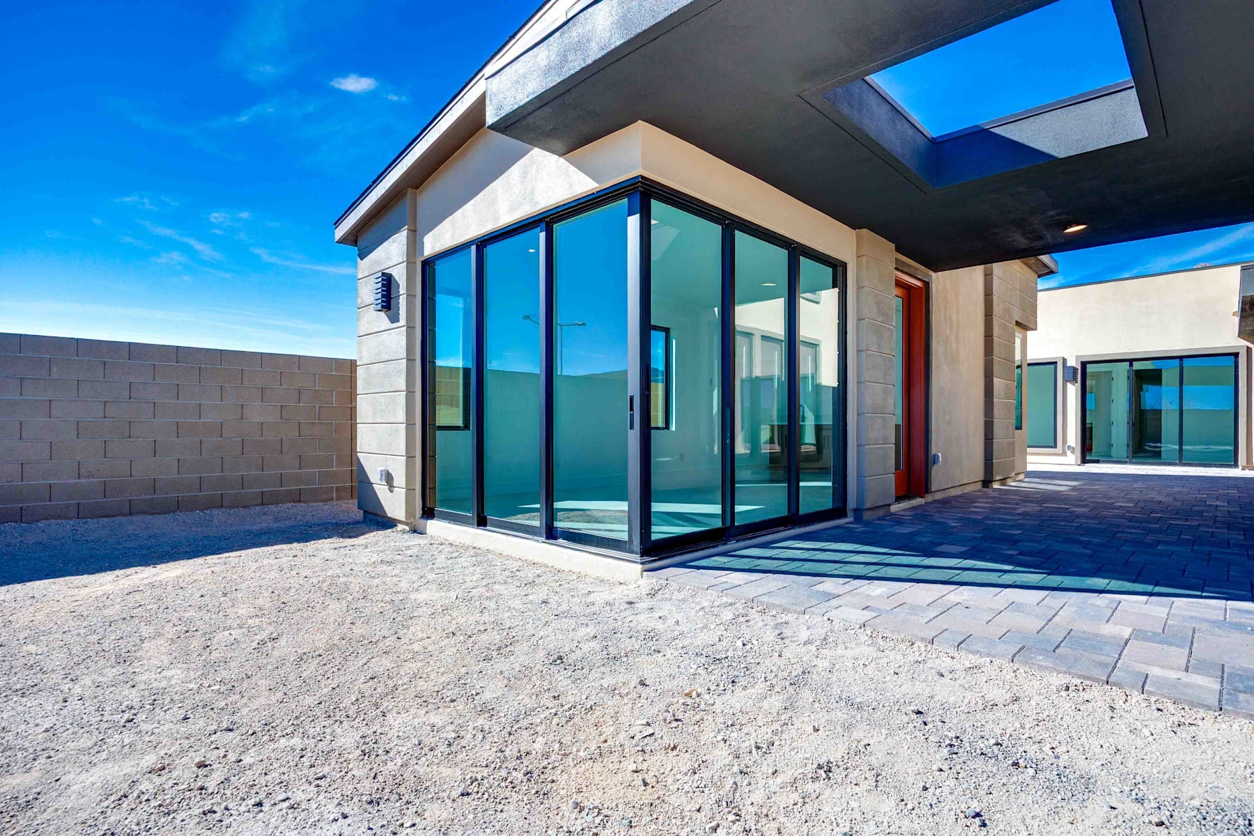 A modern, glass-enclosed entryway with a paved courtyard in the foreground, set against a clear blue sky in the background.