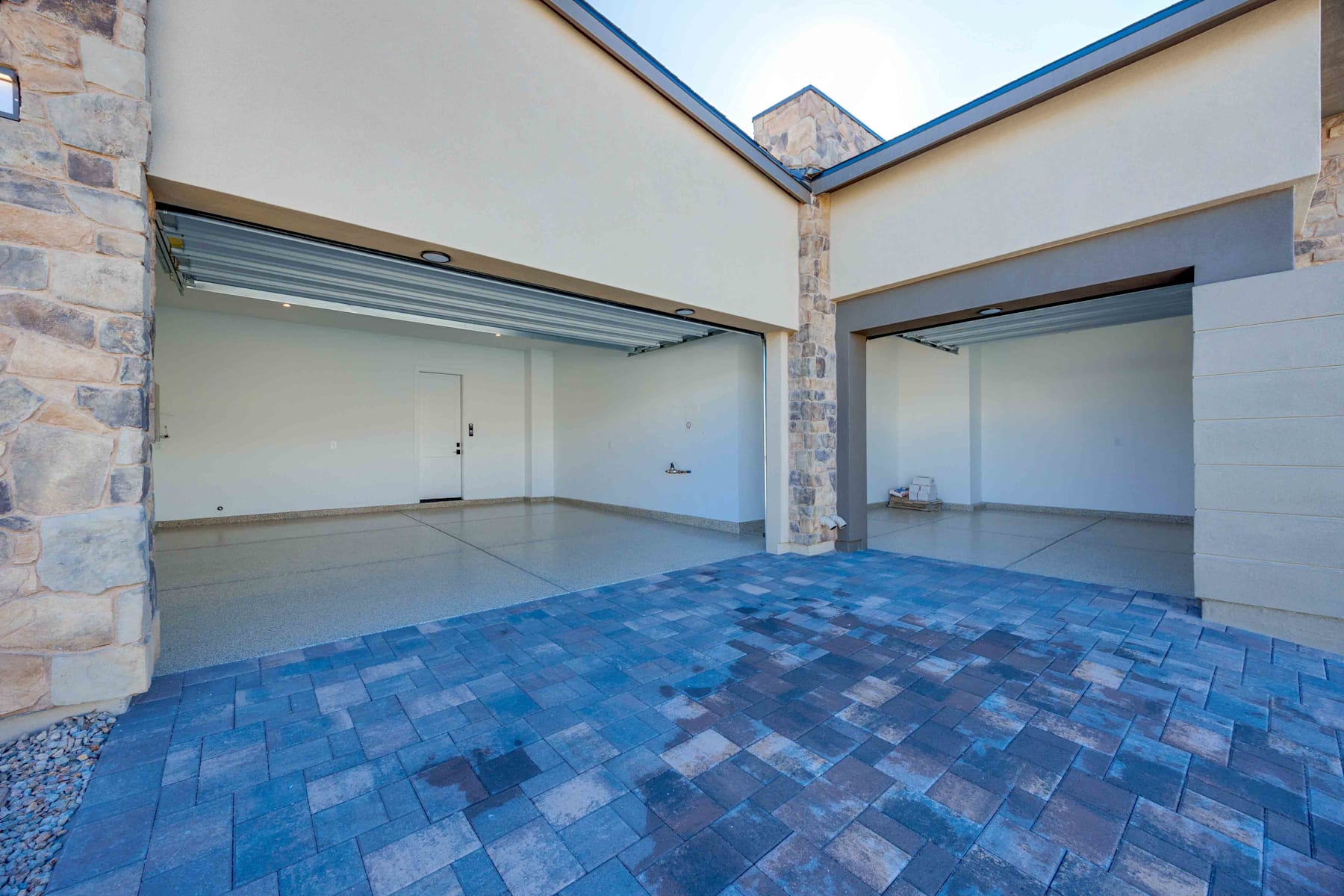 A spacious indoor area with a tiled blue floor and stone walls, featuring large sliding doors and a high ceiling.