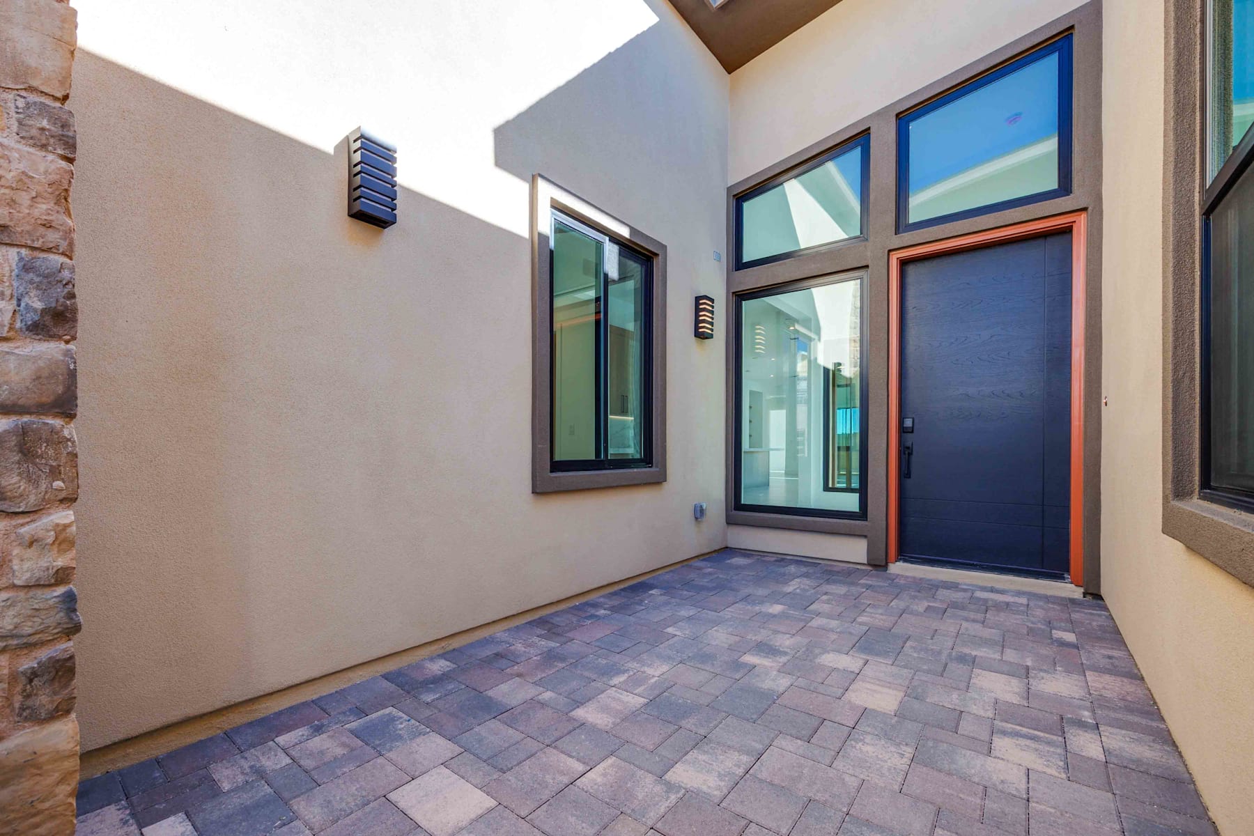A modern entryway with a paved brick floor, large windows, and a wooden door leading into the building.