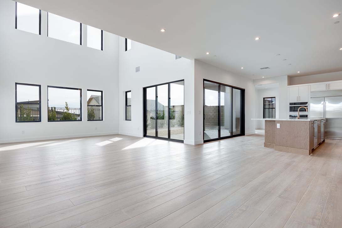 A spacious, modern interior with large windows, hardwood floors, and a kitchen visible in the background.