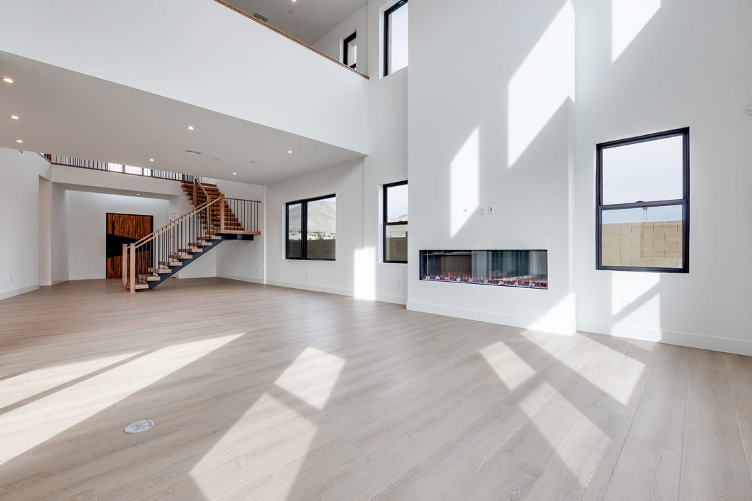 A spacious and bright interior with a modern fireplace, wooden stairs, and large windows allowing natural light to flood the room.
