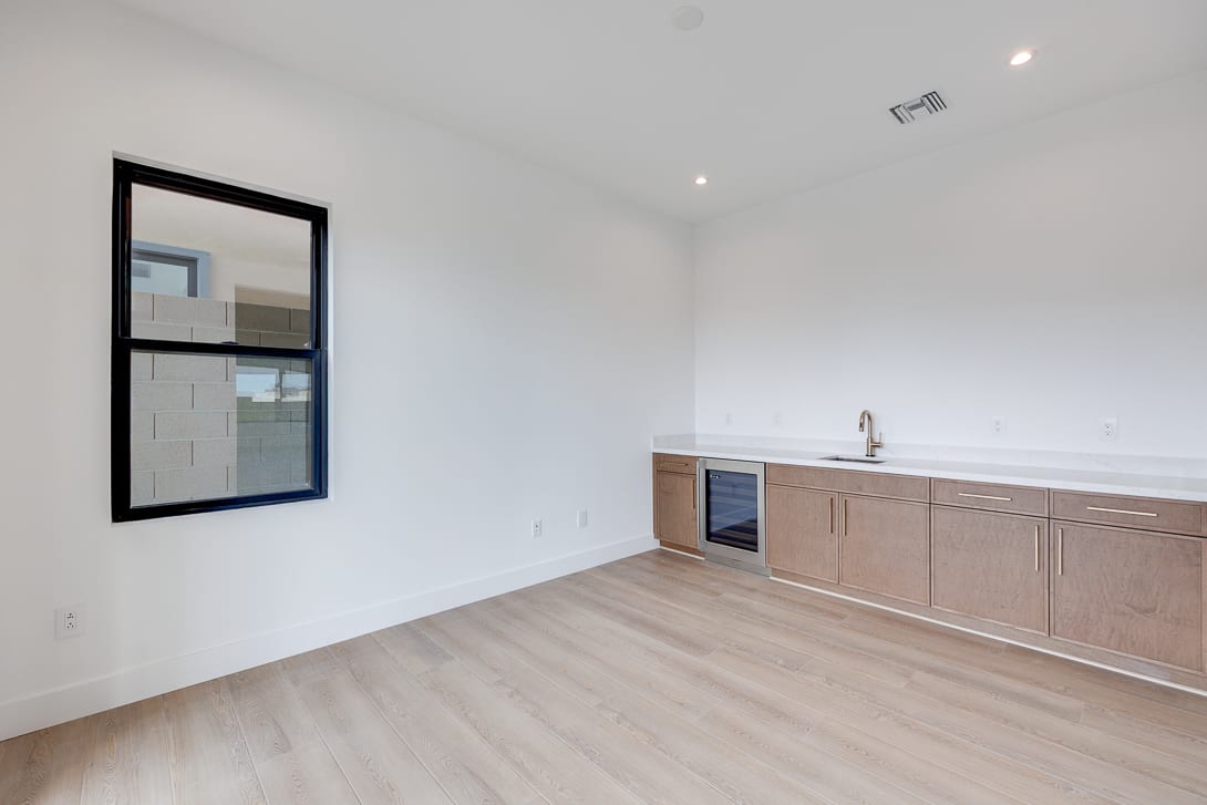 A modern, minimalist kitchen with light-colored wood cabinets, a white countertop, and a large mirror on the wall.