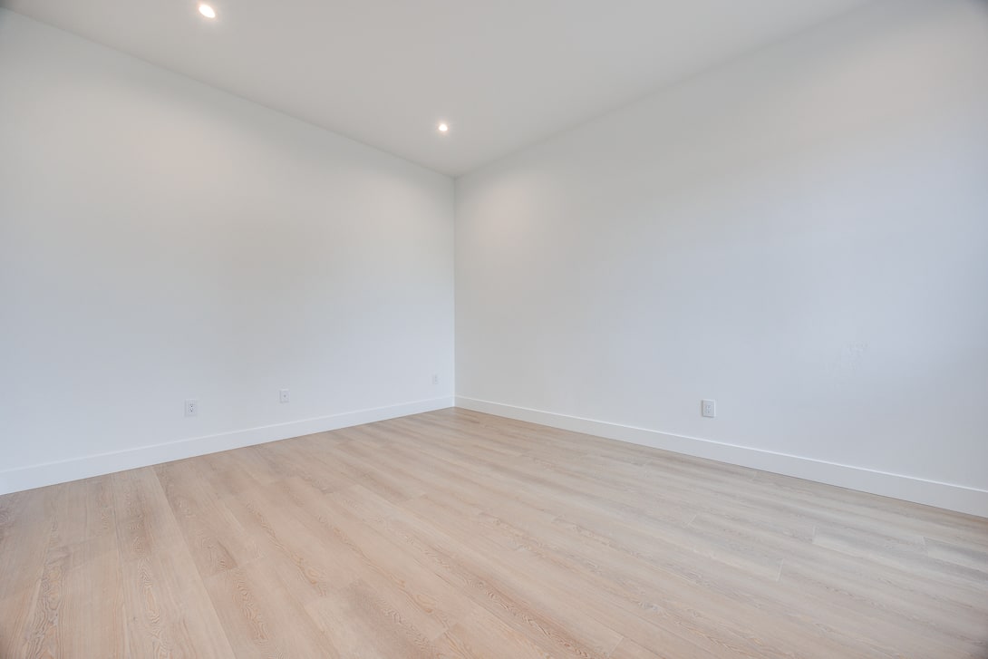 A bright, empty room with white walls and a hardwood floor, creating a clean and minimalist atmosphere.
