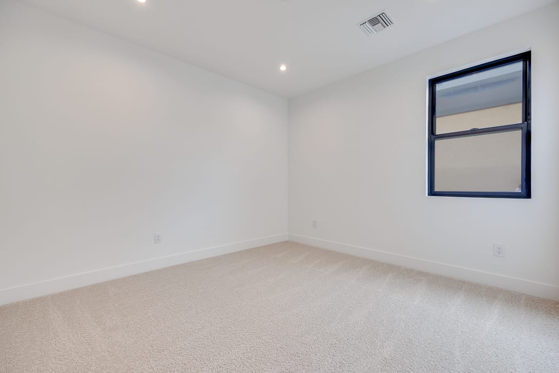 A simple, minimalist room with white walls, a large window, and a carpeted floor.