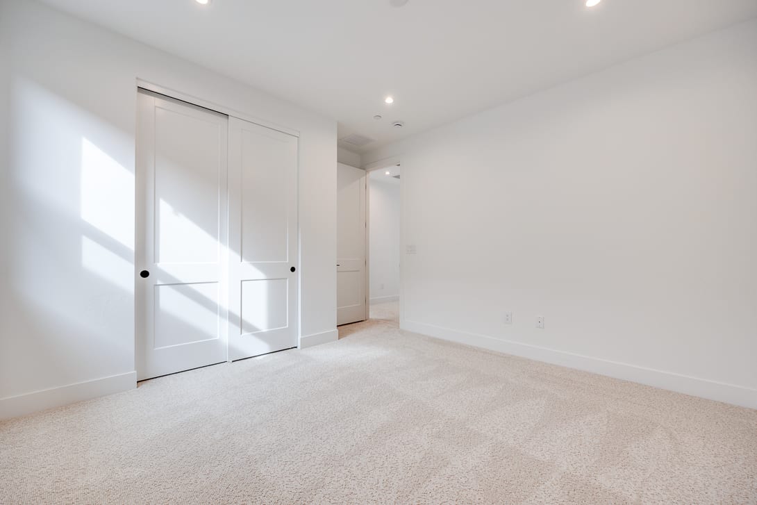 A bright, spacious room with white walls, a carpeted floor, and a closet door visible in the foreground.