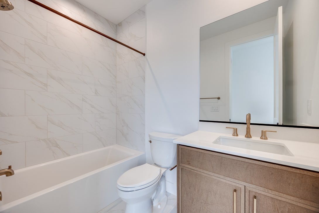 A modern and minimalist bathroom with a white marble-like wall, a wooden vanity, and a bathtub in the foreground.