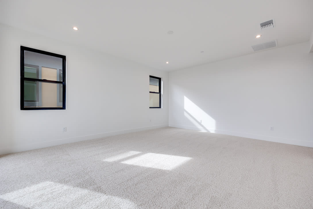 A bright, minimalist room with white walls, a large window, and a carpeted floor.
