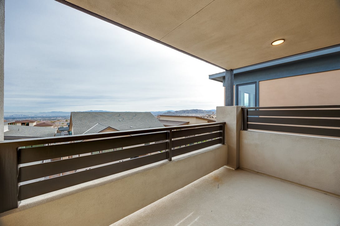 A modern balcony with a glass railing overlooks a scenic landscape in the background, featuring mountains and a cloudy sky.
