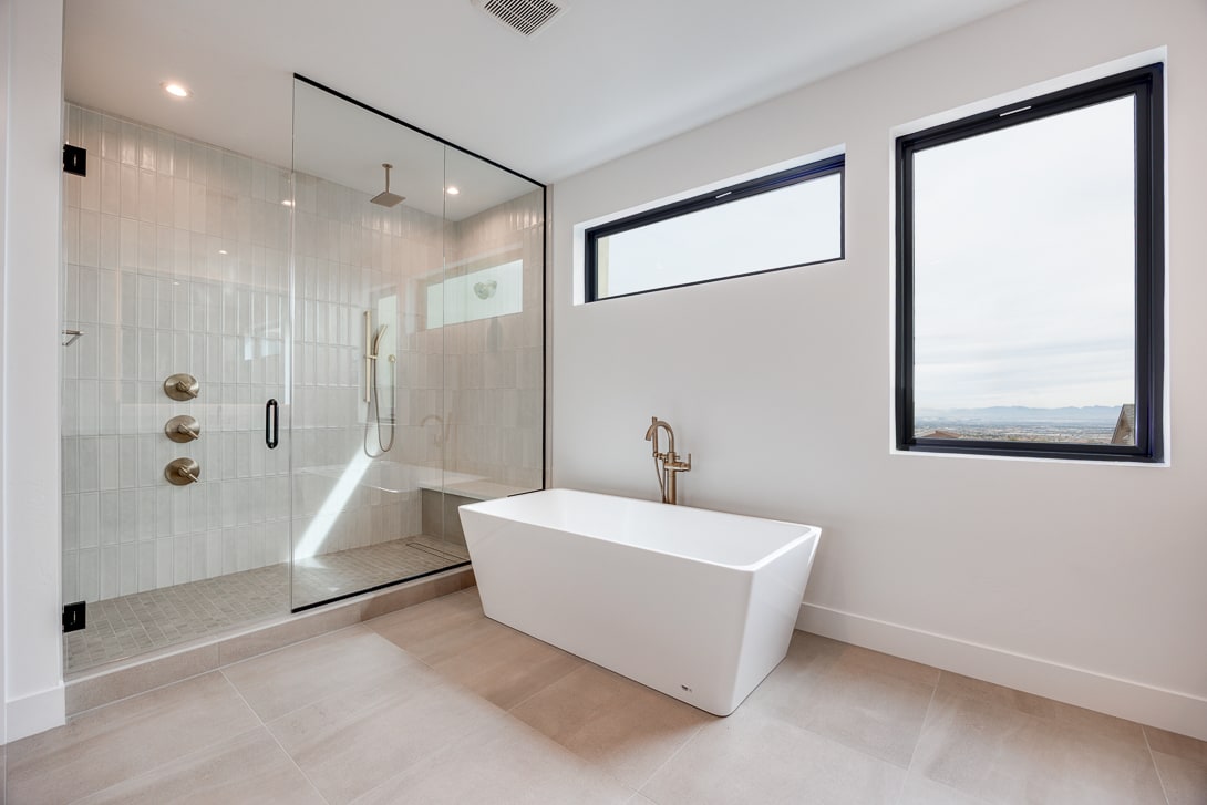 A modern, minimalist bathroom with a freestanding bathtub, glass shower enclosure, and large window providing natural light and a scenic view.
