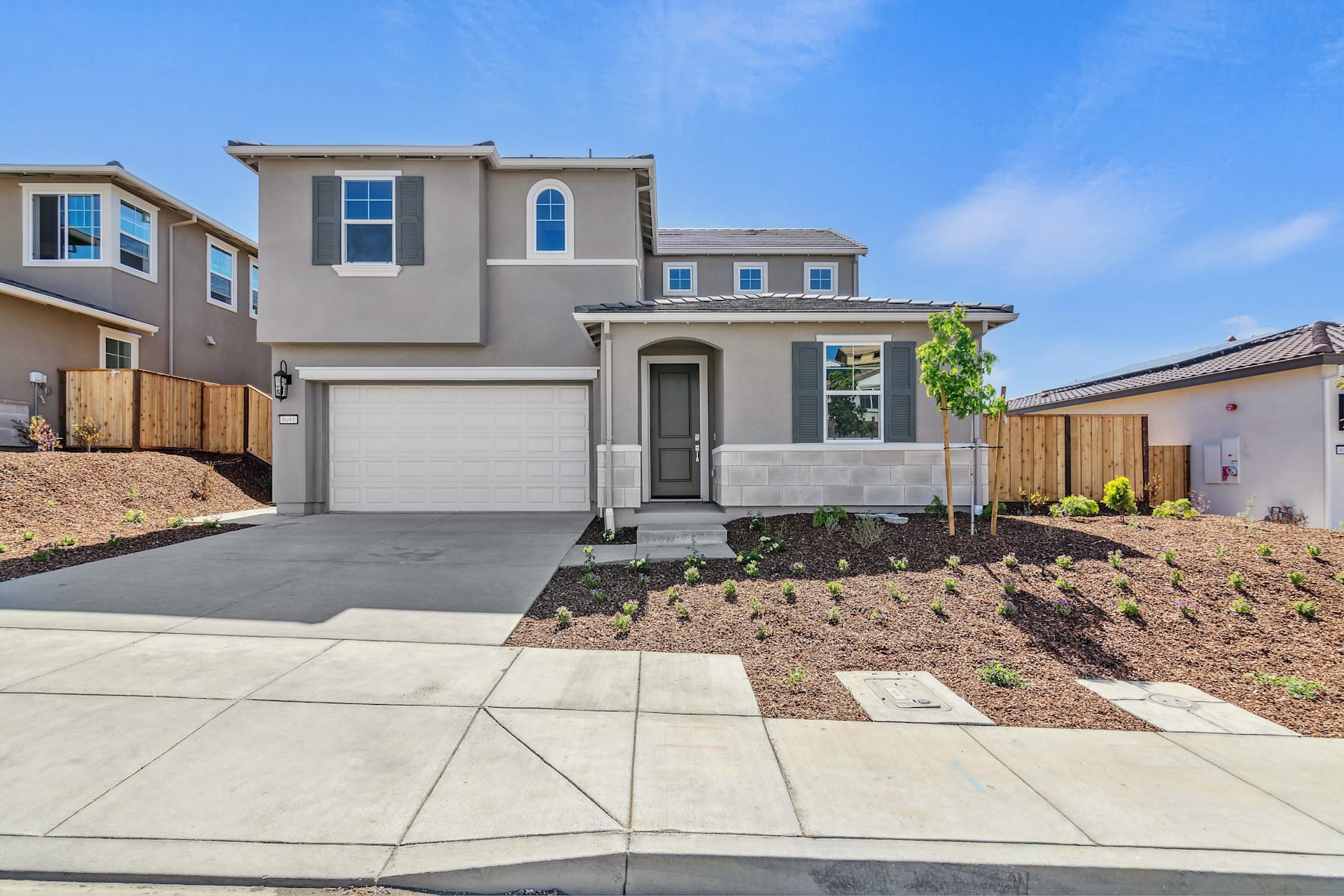 A two-story residential house with a gray exterior, a garage, and a landscaped front yard with a concrete walkway leading to the entrance.