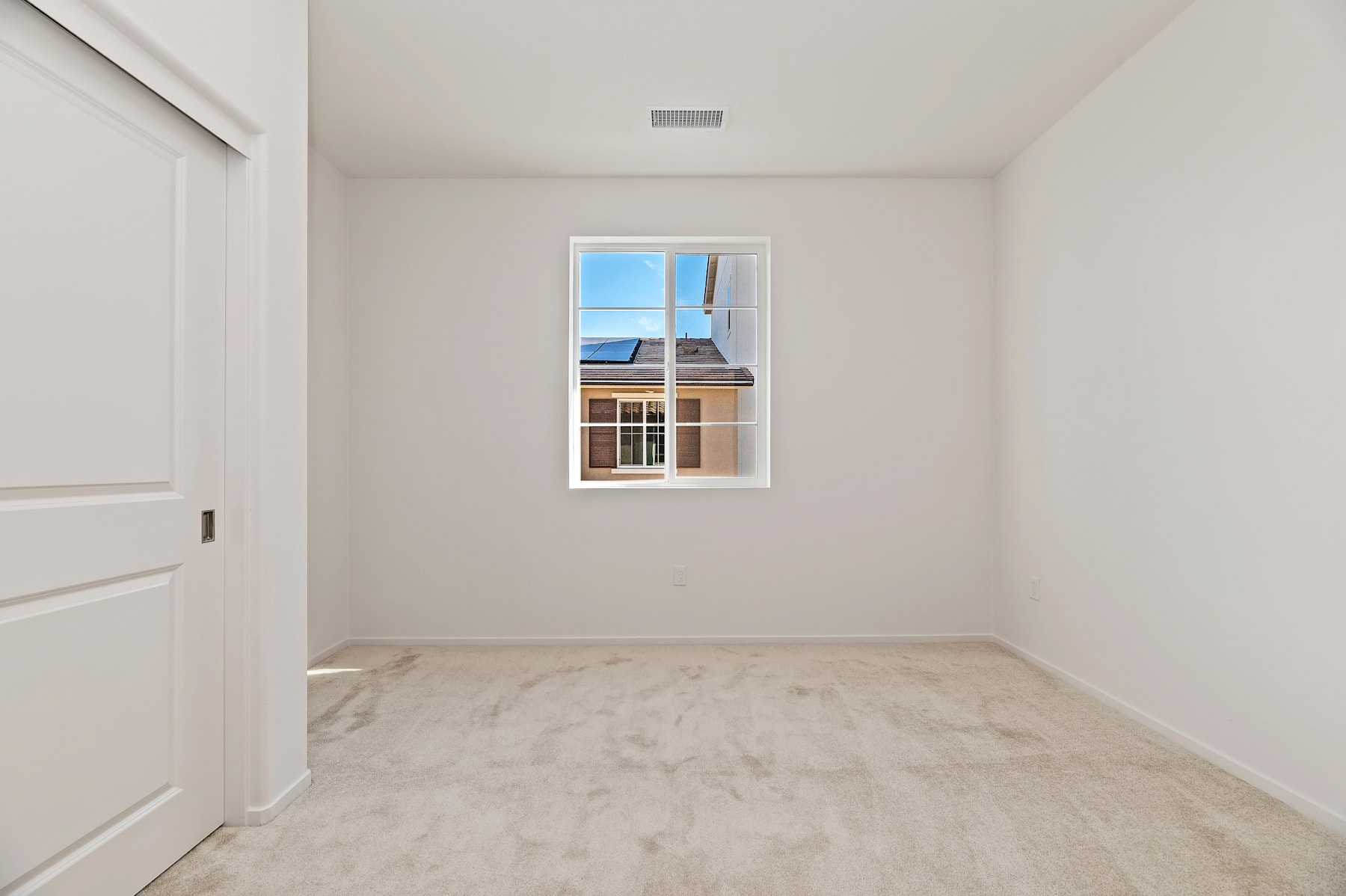 A bright, empty room with a window overlooking a residential area, featuring a white floor and walls.