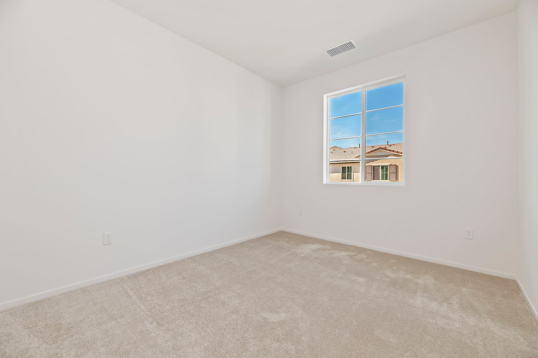A bright, empty room with a large window overlooking a residential neighborhood in the background.