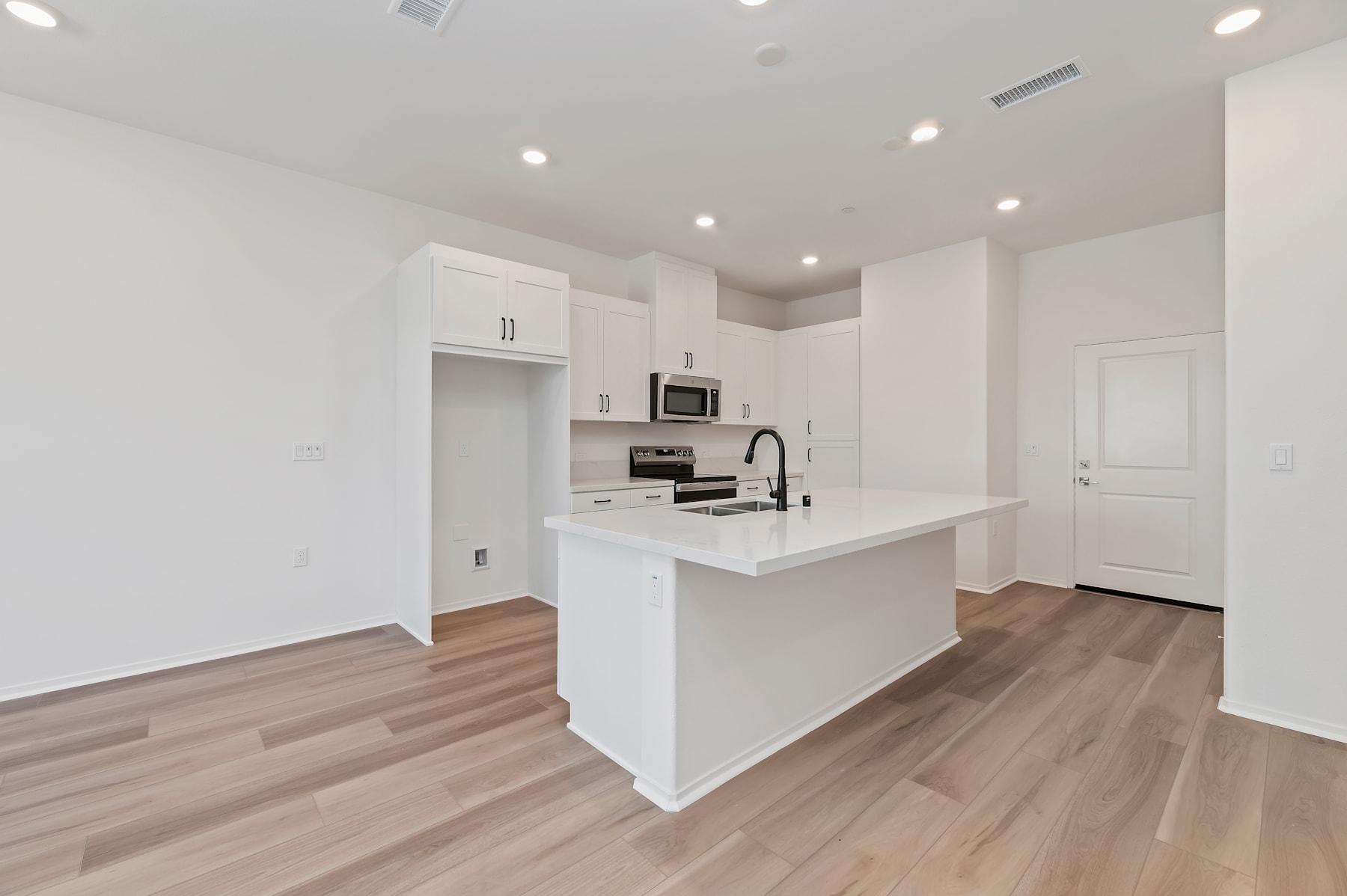 A modern, minimalist kitchen with white cabinets, a white countertop, and hardwood floors, set against a bright and airy background.