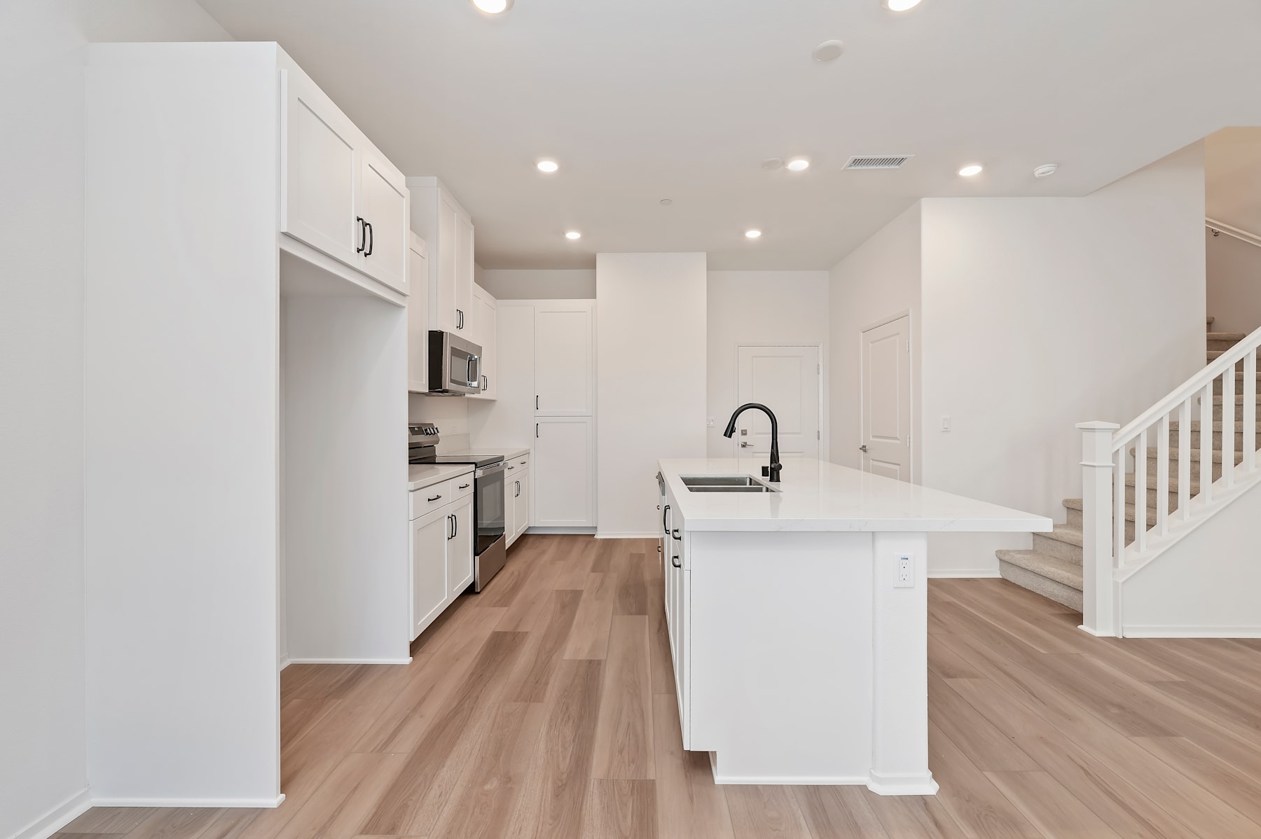 A modern, open-concept kitchen with white cabinets, a central island, and hardwood flooring, creating a bright and spacious living environment.