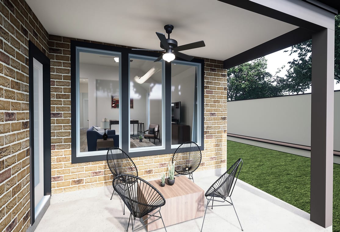 A covered patio with a brick exterior, featuring a ceiling fan, glass doors, and outdoor furniture on a grassy lawn.