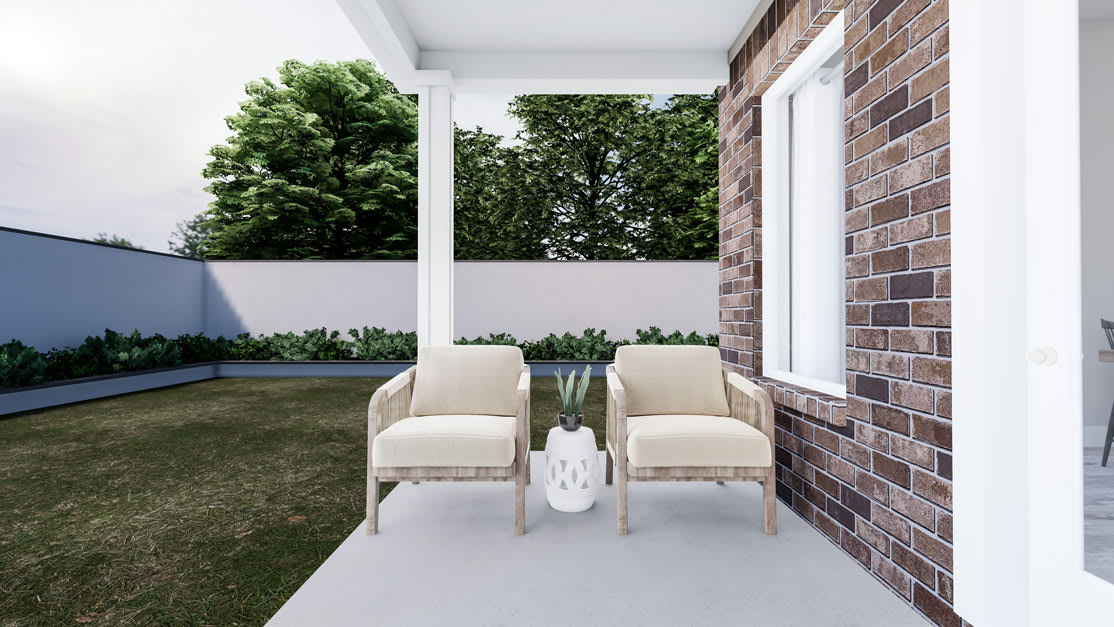 A cozy outdoor seating area with two white armchairs on a concrete patio, surrounded by lush greenery and a brick wall in the background.