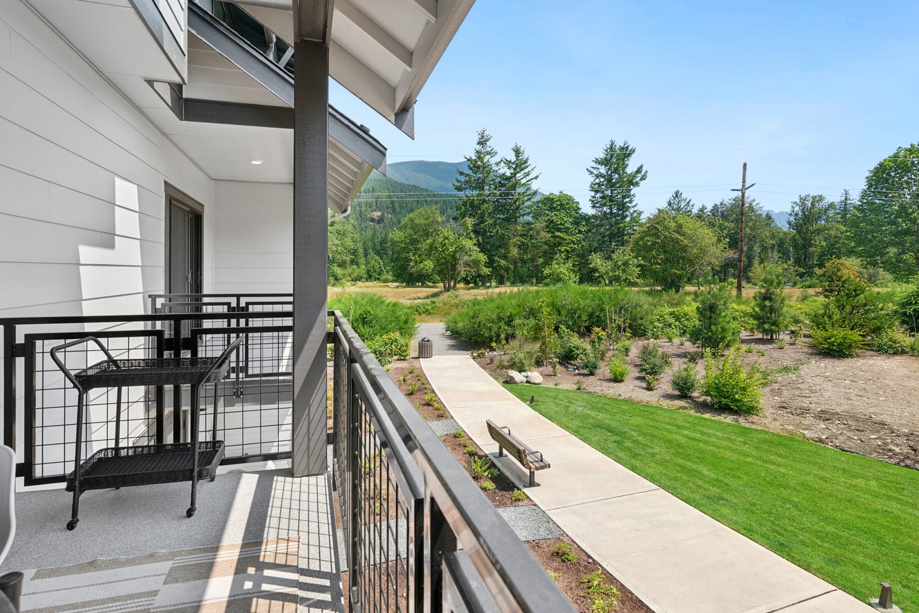 A modern, multi-story building with a balcony overlooking a well-manicured lawn and a lush, forested landscape in the background.