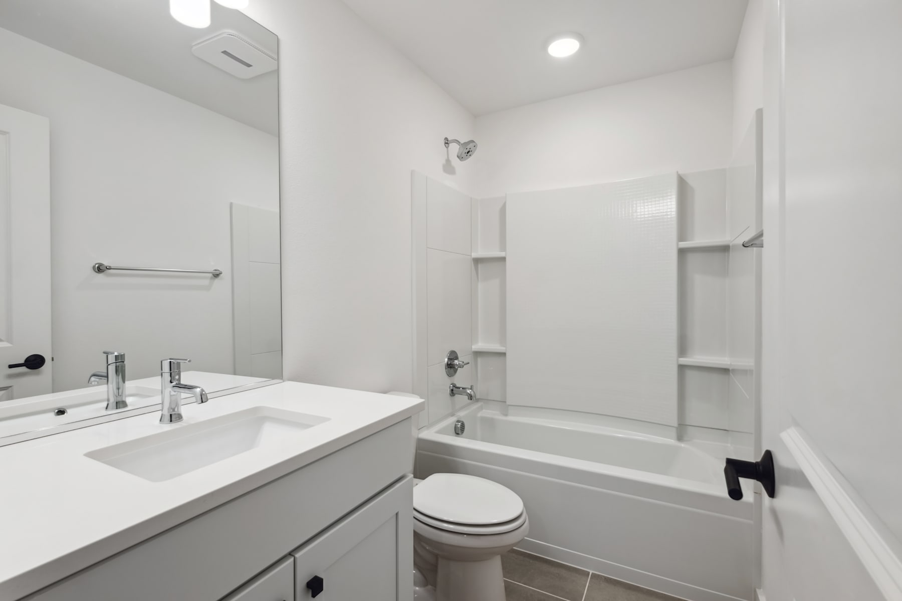 A modern, minimalist bathroom with a white vanity, a bathtub, and recessed lighting fixtures on the ceiling.